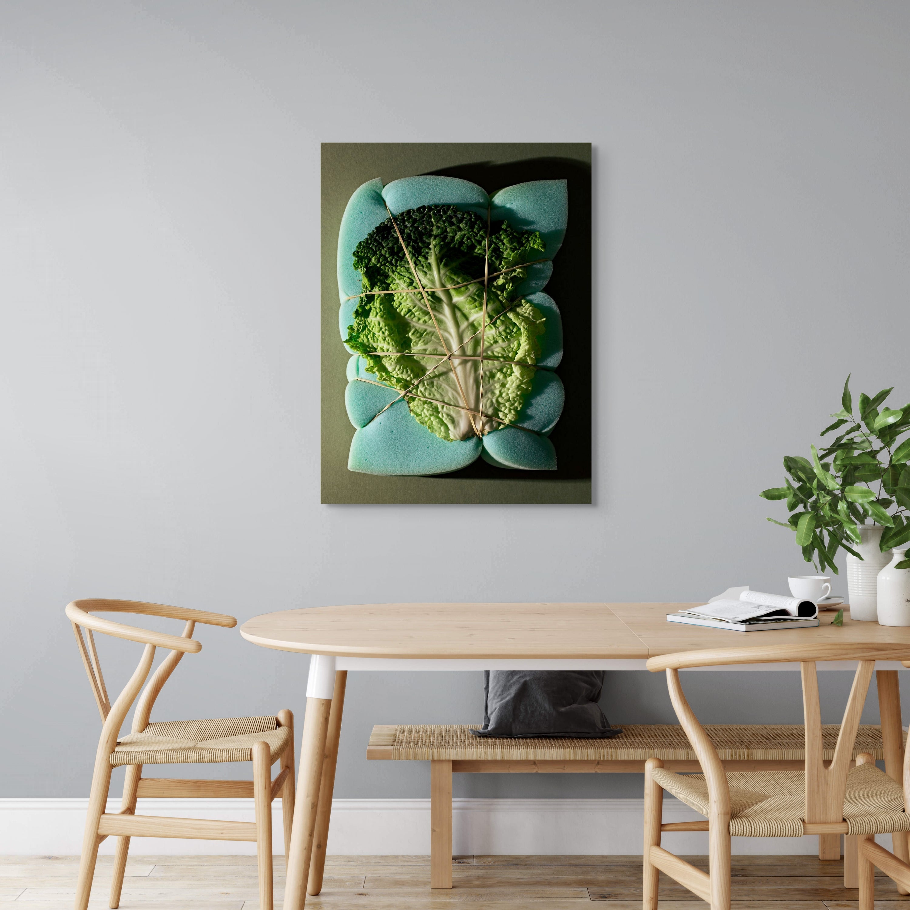Metal print of a cabbage leaf displayed above a light wood dining table.