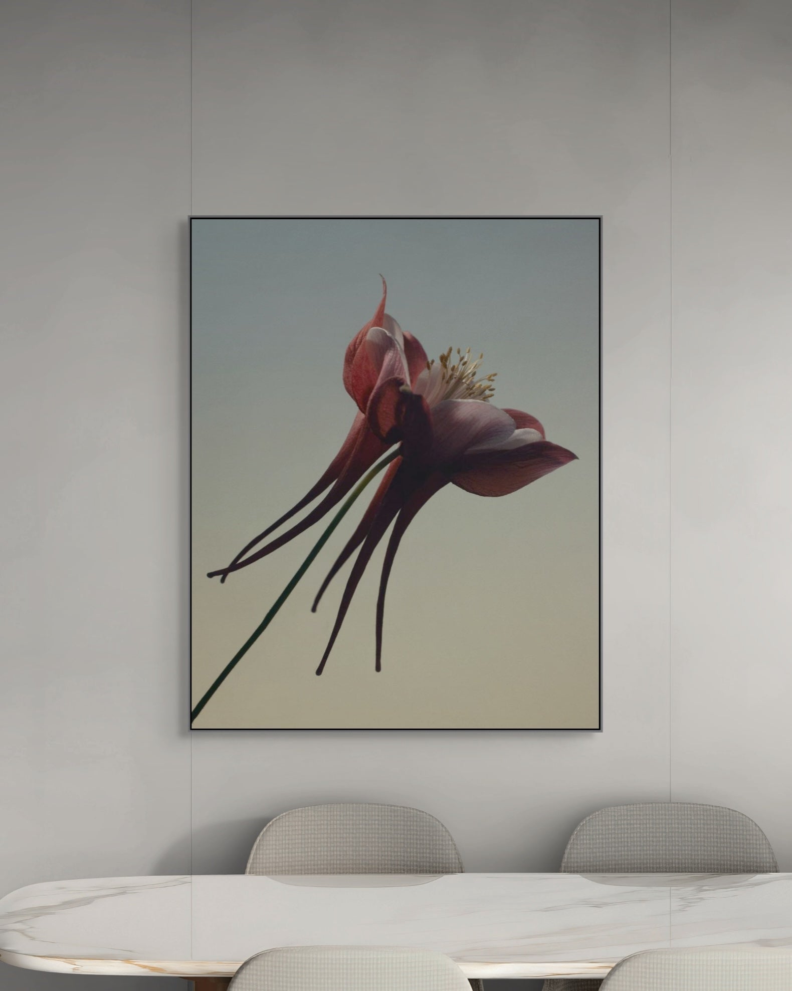 Framed botanical artwork of a red flower on a wall above a dining table.