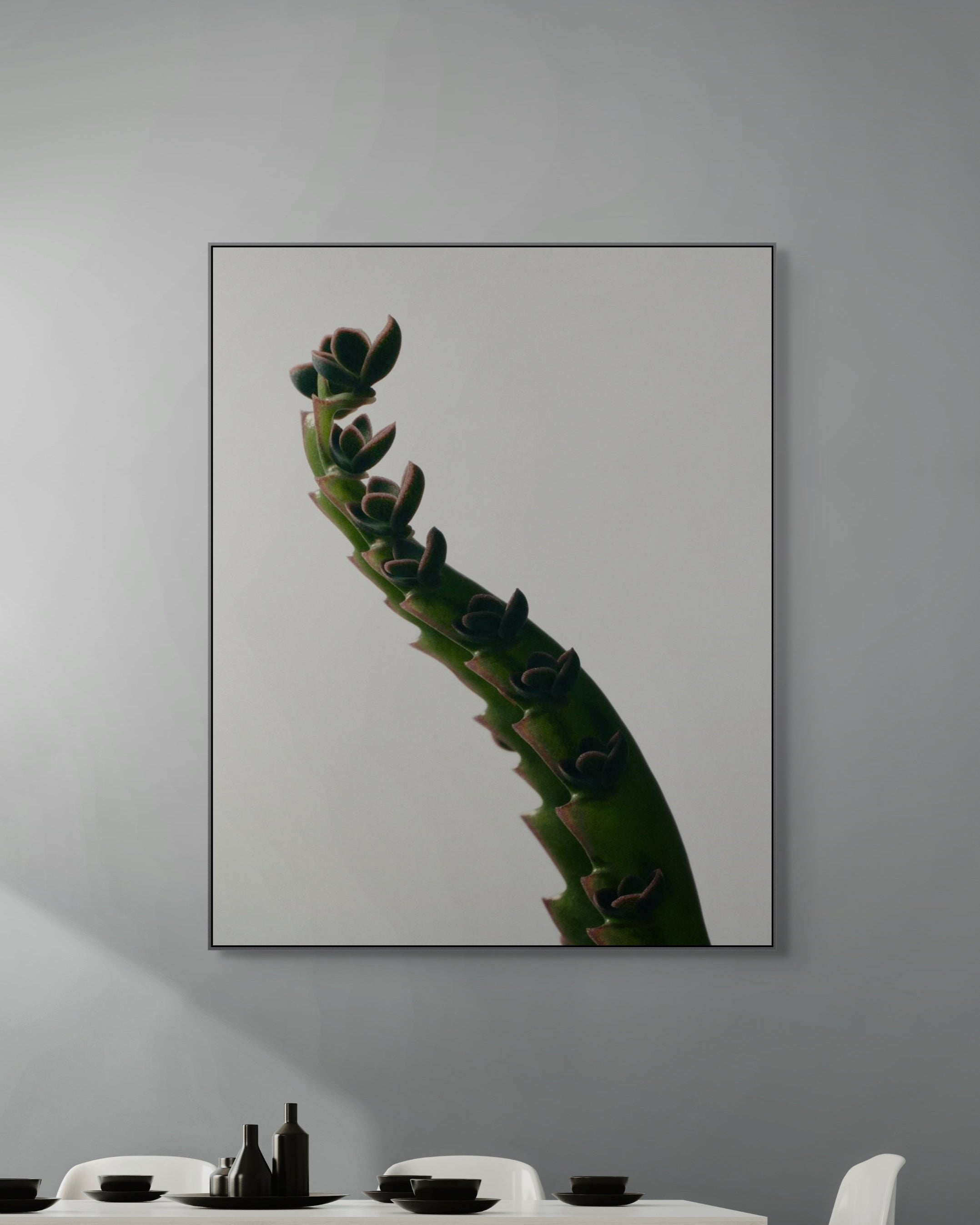 Framed artwork of a cactus on a gray wall above a dining table.