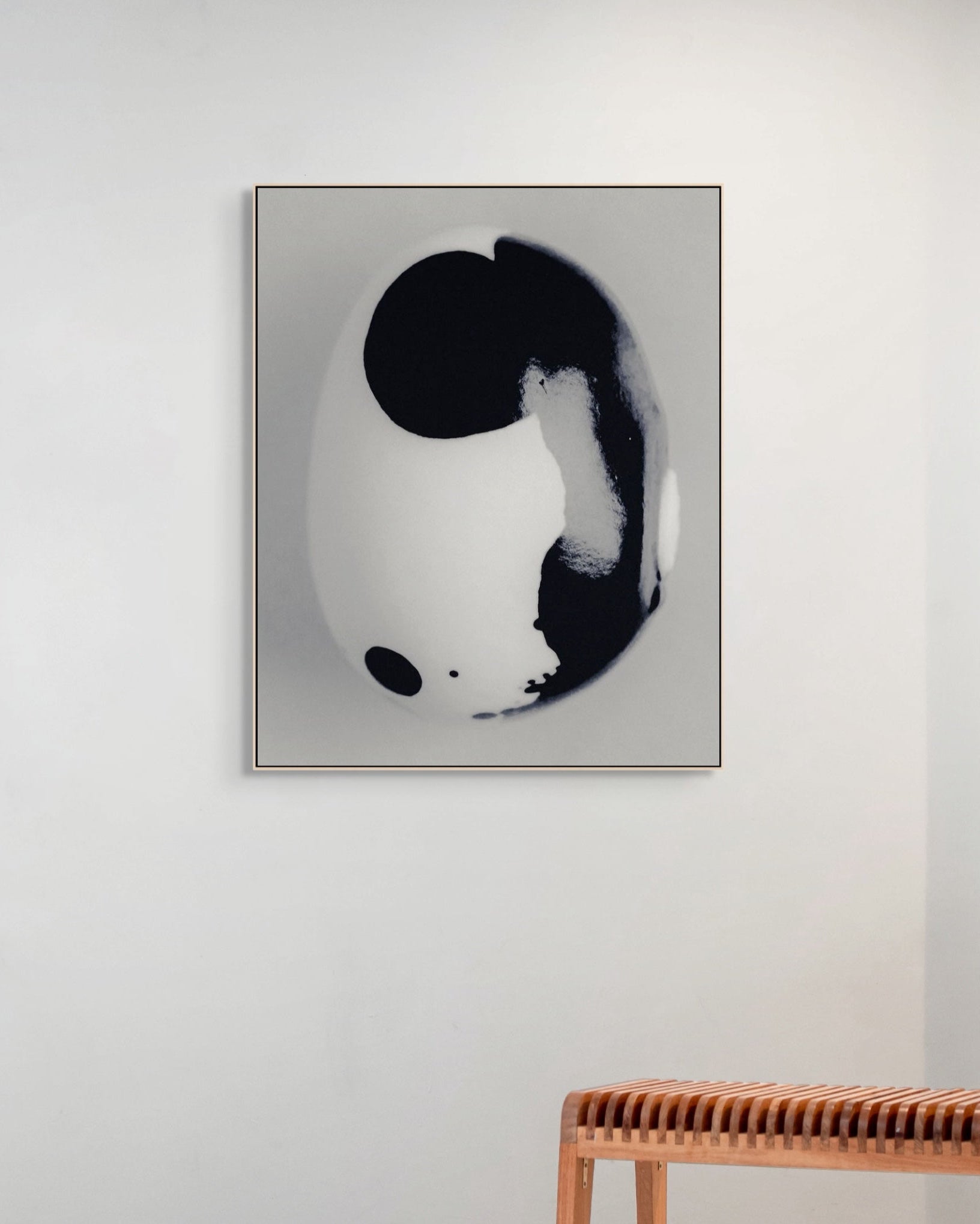Framed black and white abstract art piece on a wall with a wooden bench below.