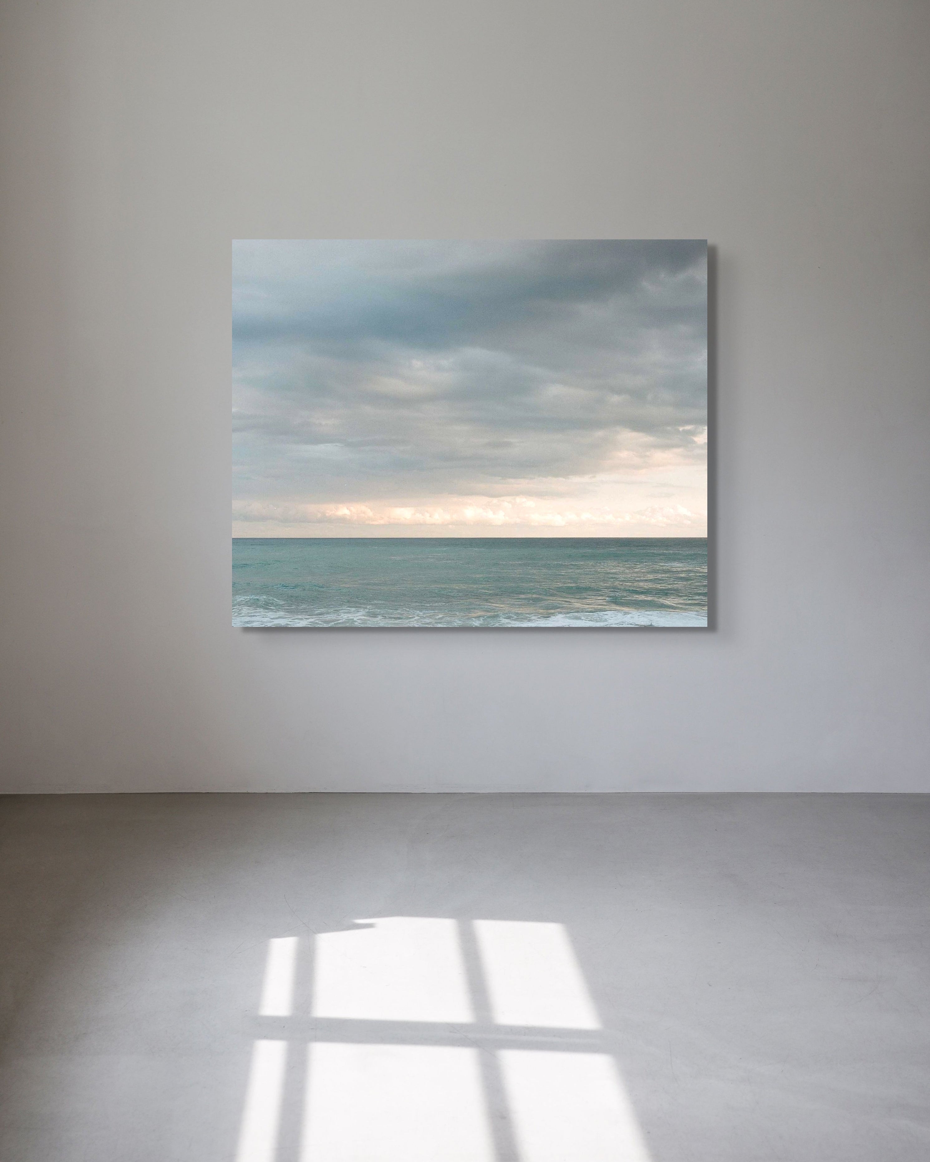Seascape photograph by Mark Forbes displayed on a light grey wall in a minimal room with soft natural light on the floor.