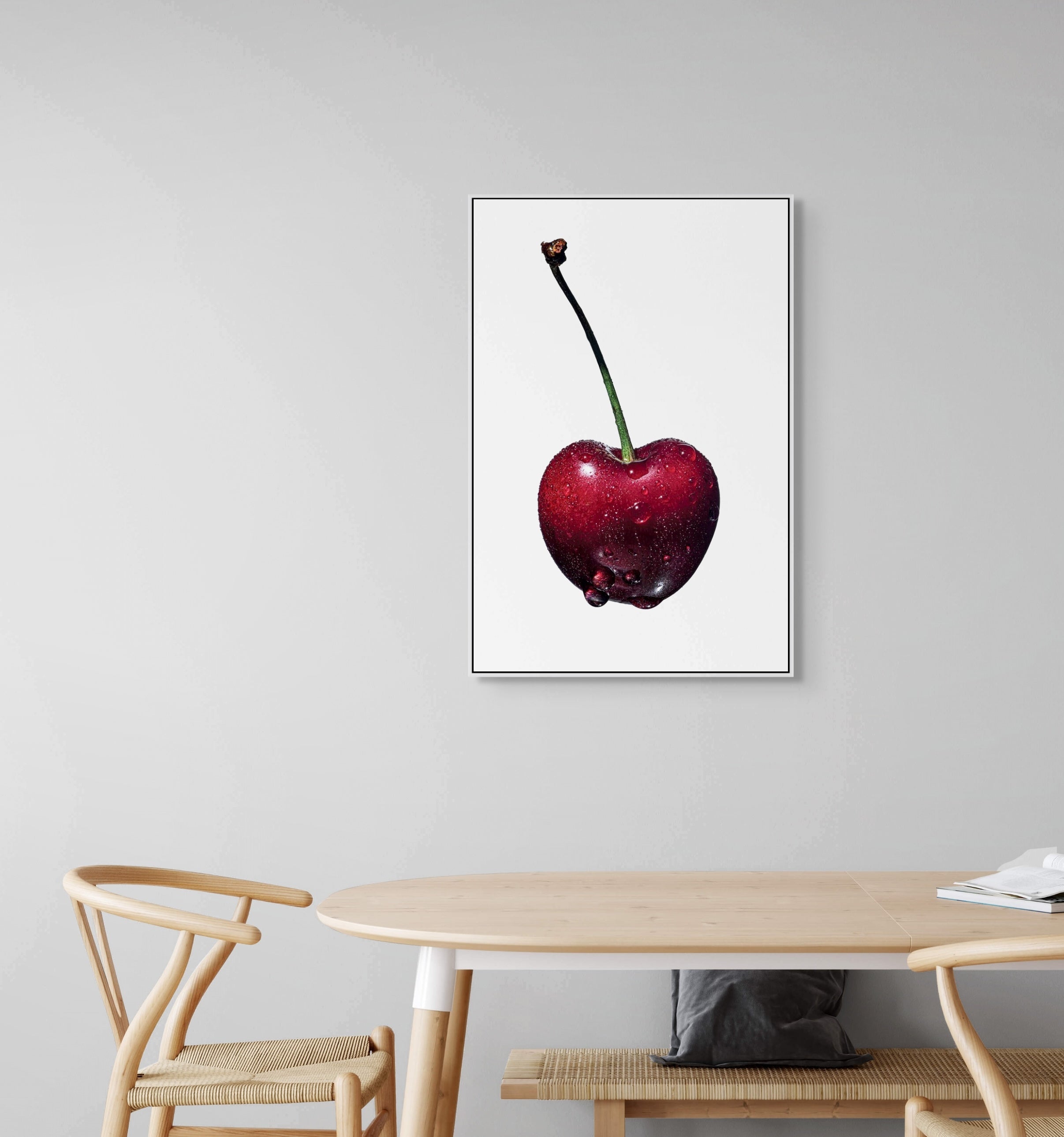 Framed artwork of a red cherry on a gray wall above a wooden table.