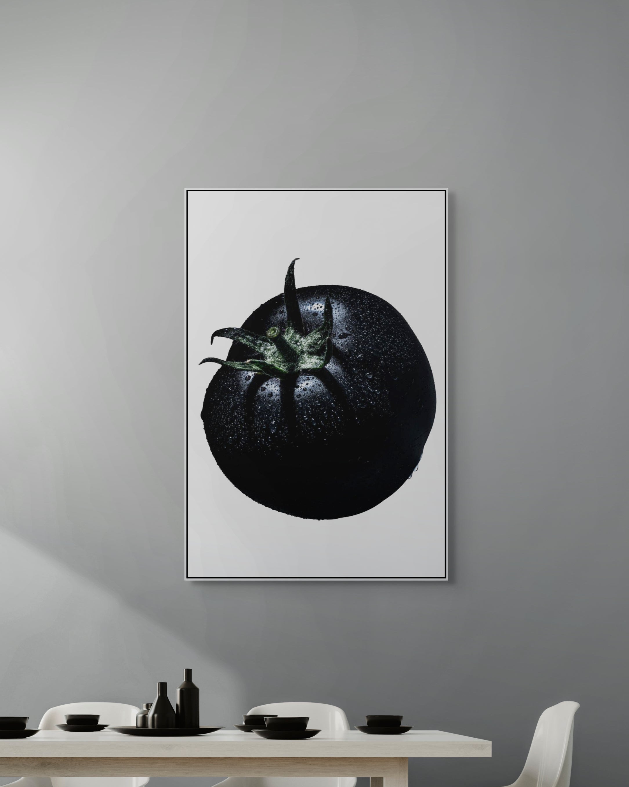 Framed artwork of a black tomato on a gray wall above a dining table.