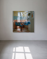 Square metal print reflecting a room with chairs and a table on a white wall 