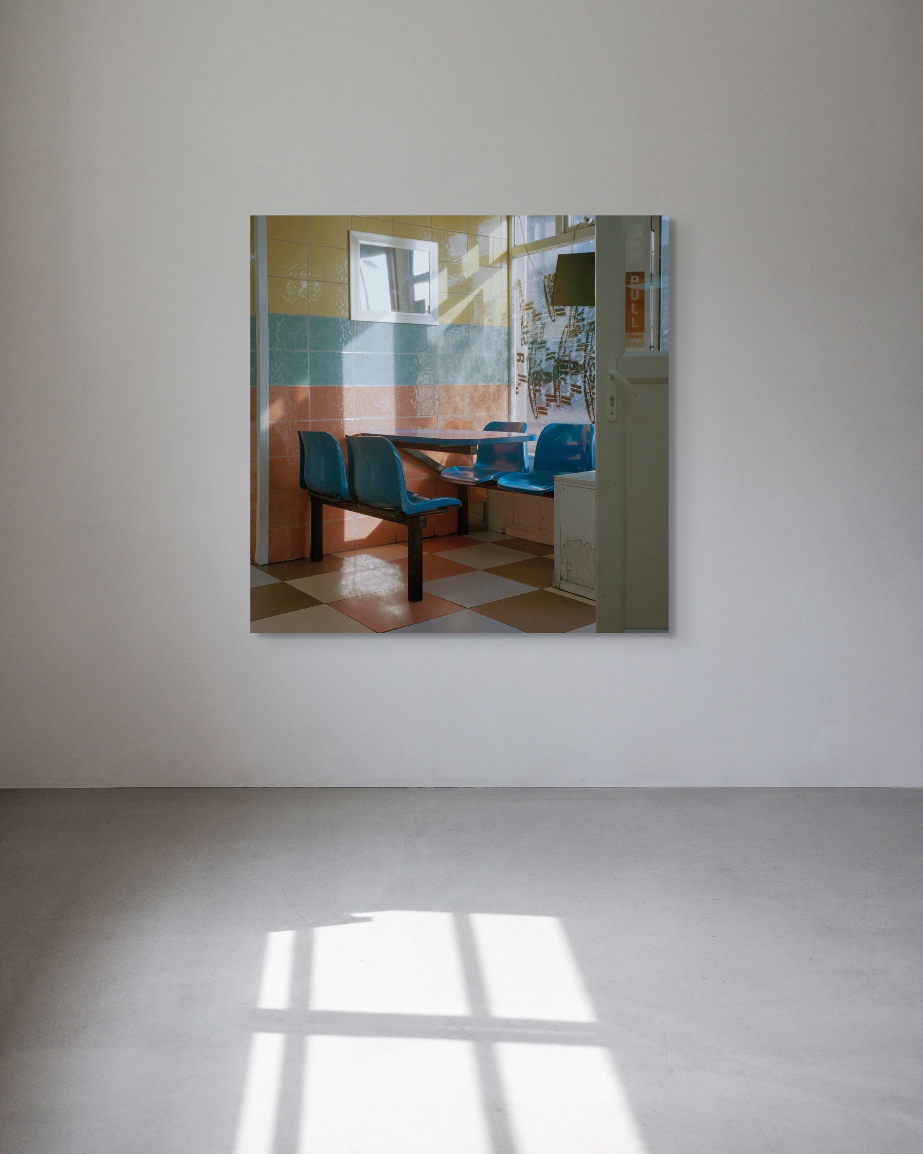 Square metal print reflecting a room with chairs and a table on a white wall 