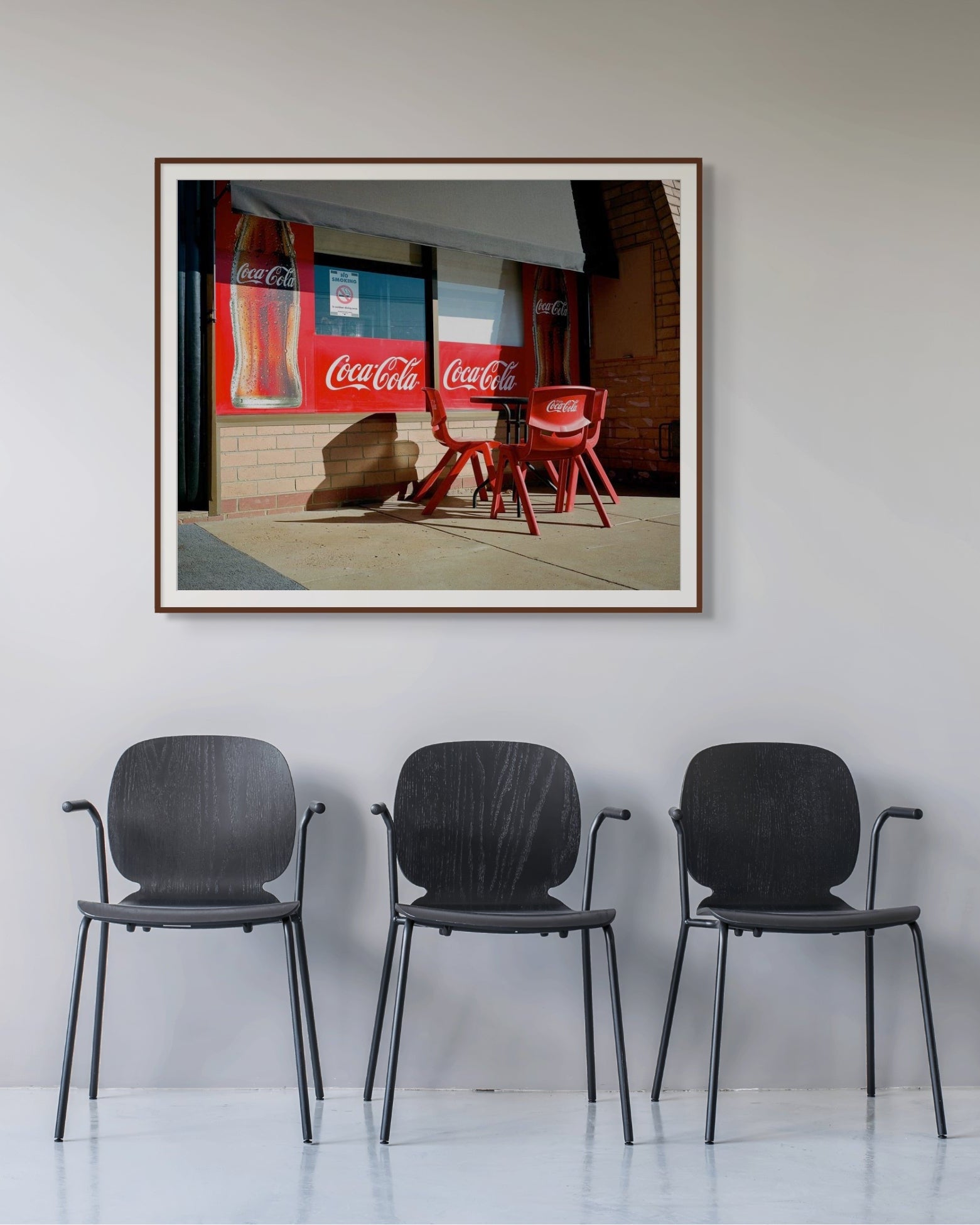 Framed Coca-Cola storefront photograph by Mark Forbes on a light grey wall above three black chairs in a contemporary waiting area.