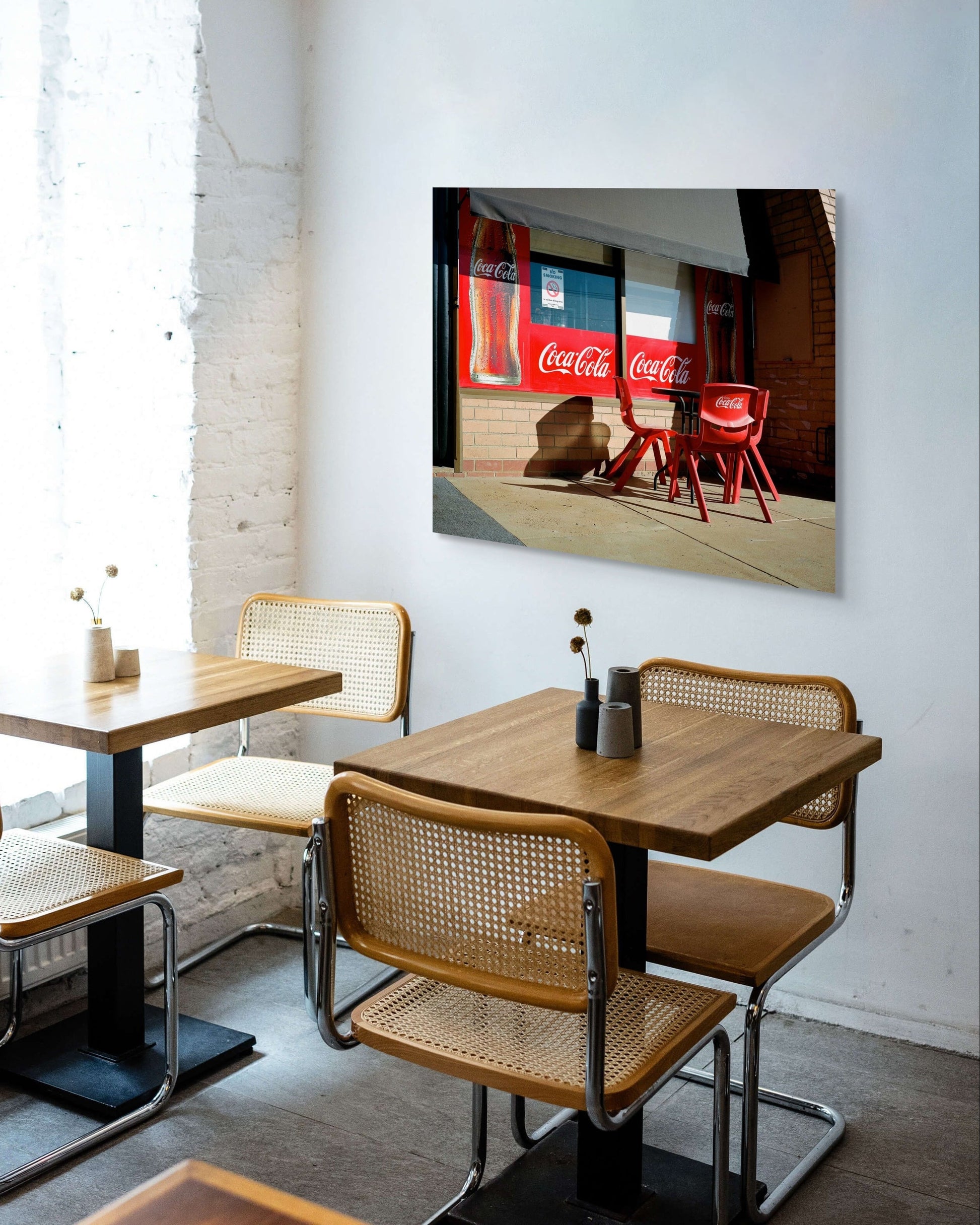 Childhood Memories’ metal print by Mark Forbes displayed in a modern café interior with wood tables and cane chairs.