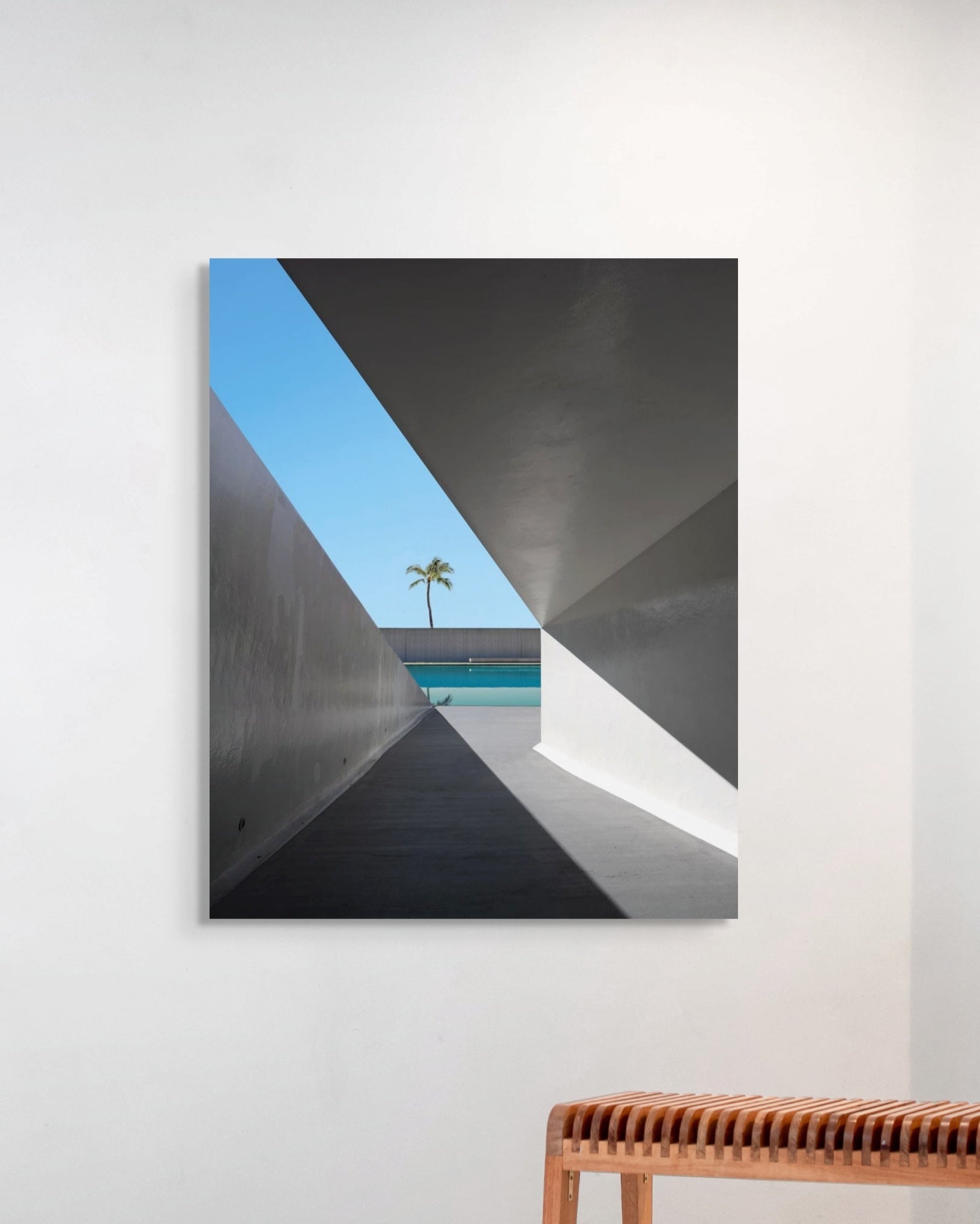 Abstract art piece with geometric shapes on a white wall above a wooden bench.