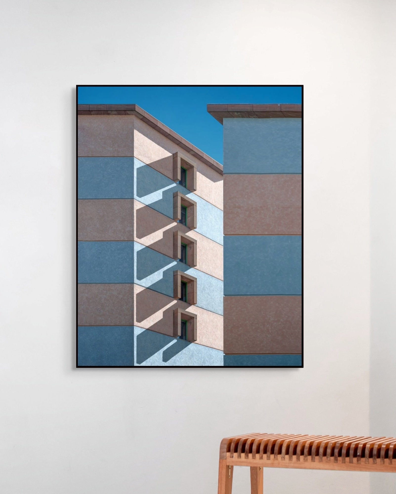 Framed abstract art of geometric shapes on a white wall with a wooden bench below.