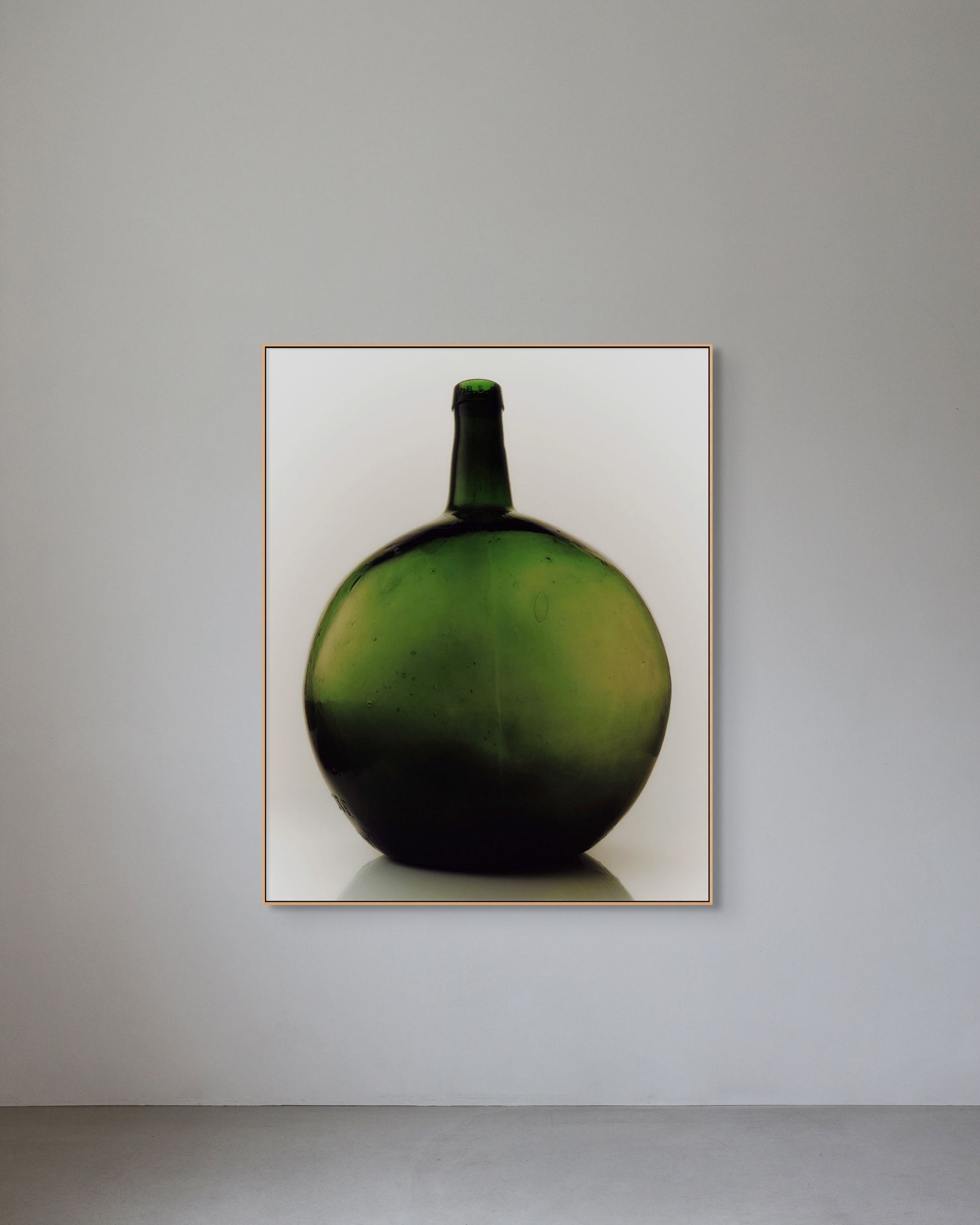Framed photograph of a green bottle on a gray wall