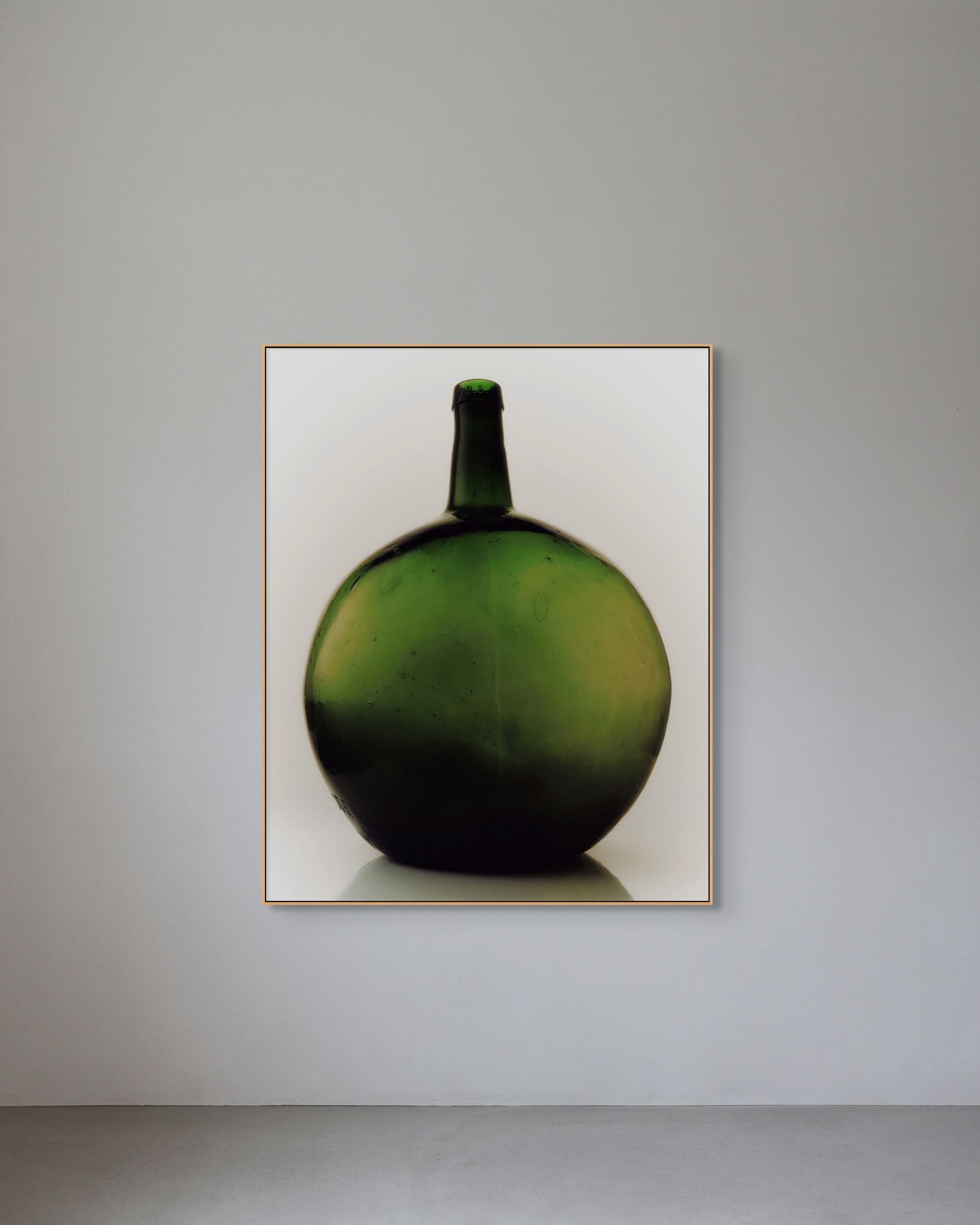 Framed photograph of a green bottle on a gray wall