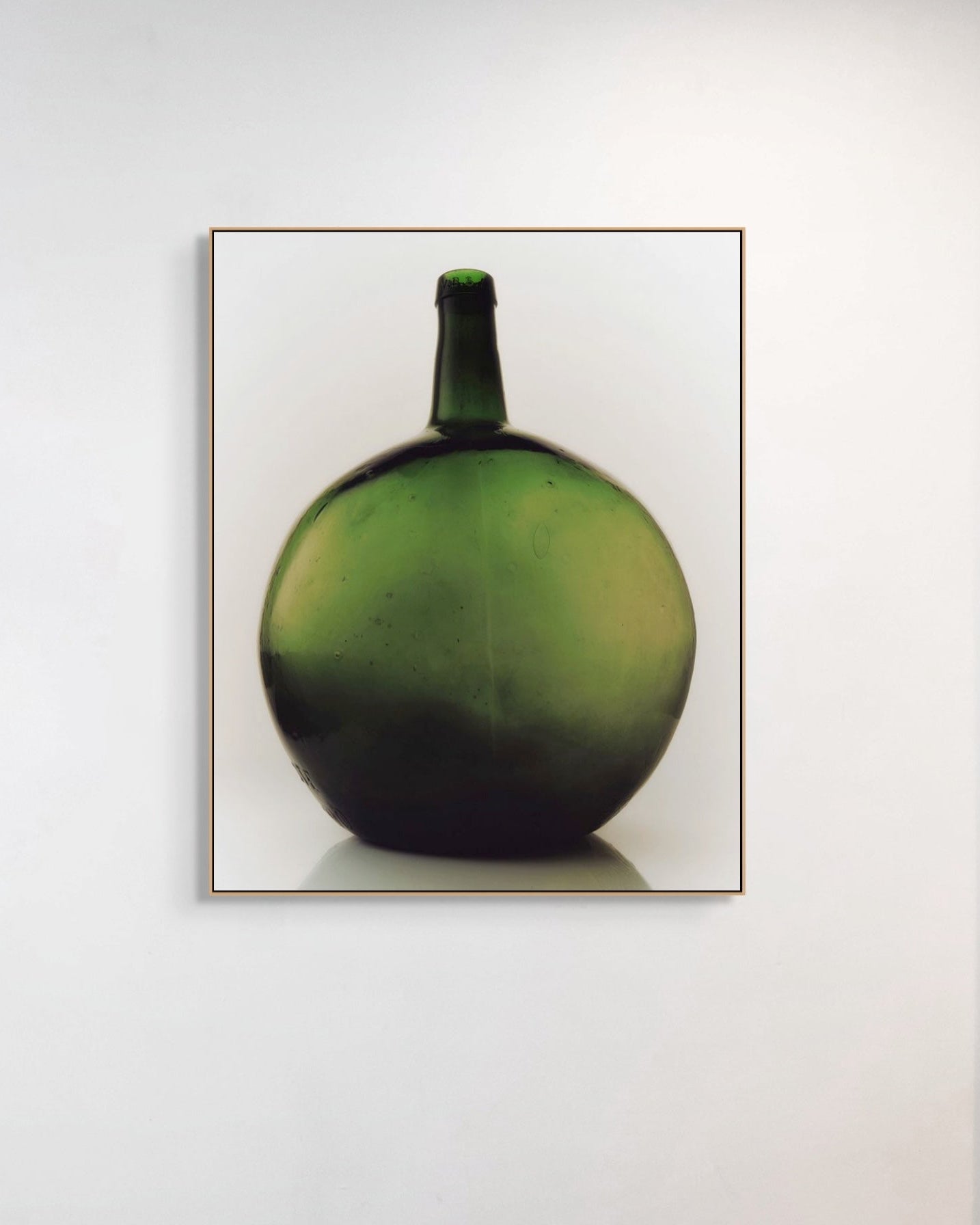 Framed photograph of a green bottle on a white wall