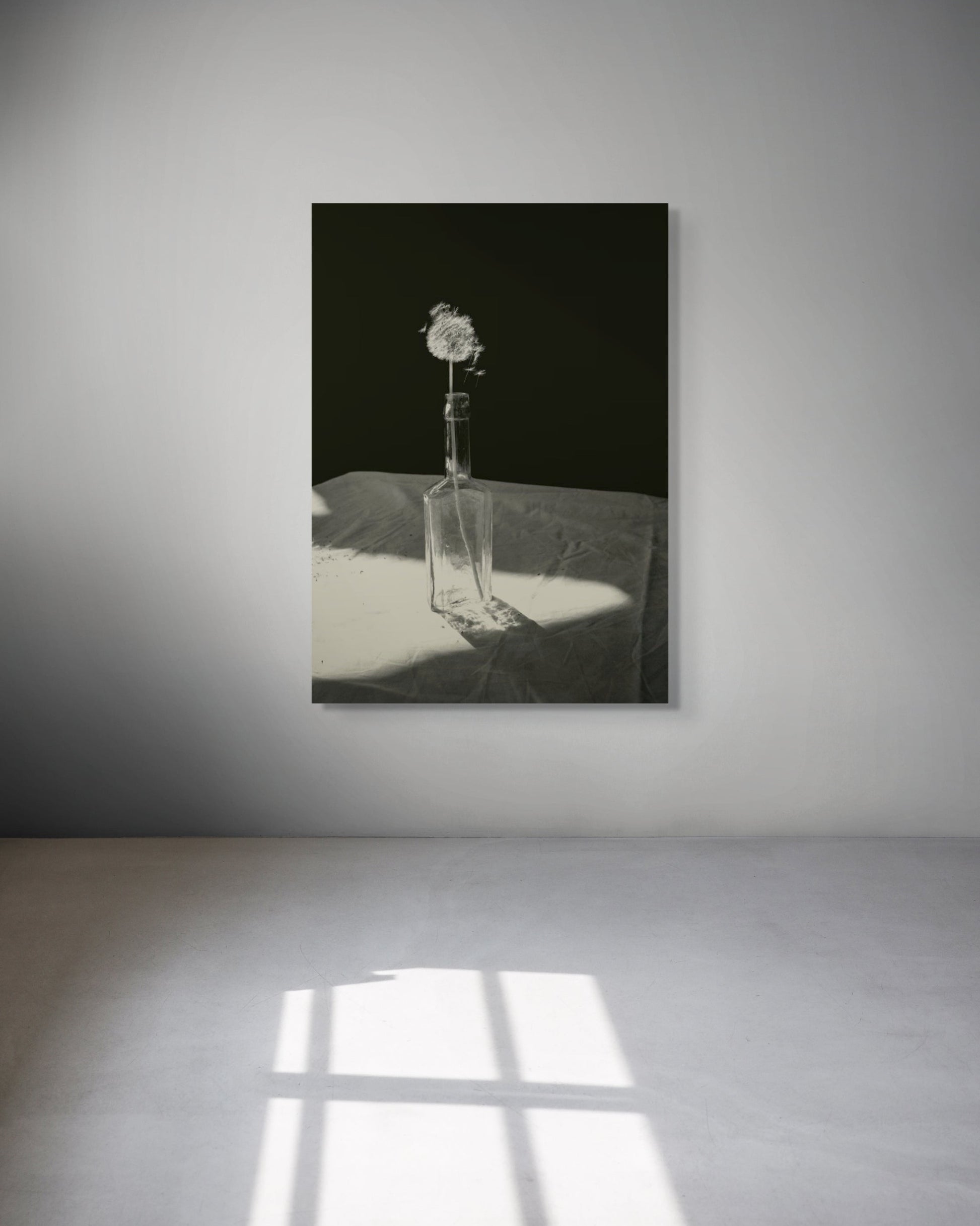 Framed black and white artwork of a flower in a glass bottle on a gray wall.
