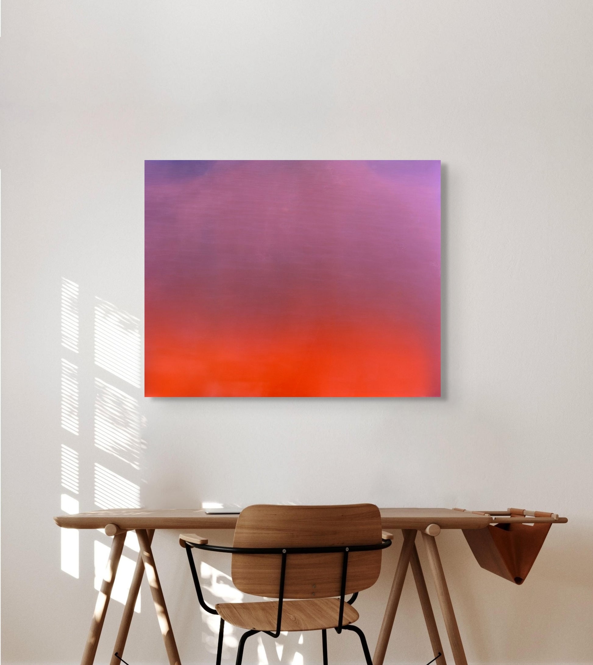 Abstract metal print on a wall above a wooden desk with a chair.