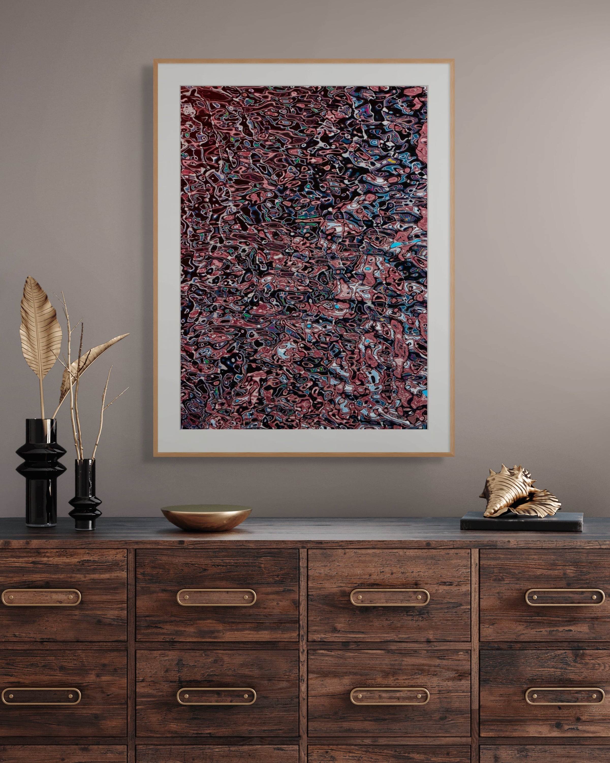 Framed abstract photograph with a white mat and gold frame displayed above a rustic wood console, featuring deep reds, blacks, and subtle blue accents in an intricate, fluid pattern.