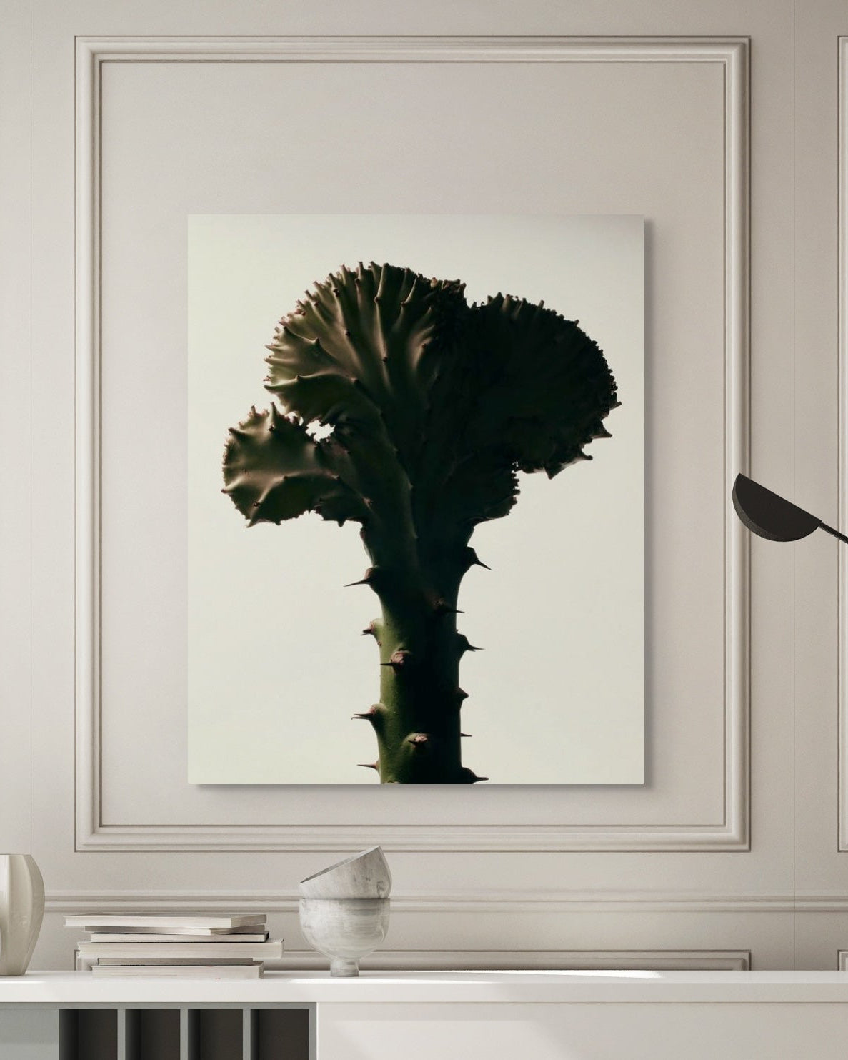 Framed artwork of a cactus on a wall with decorative elements below.