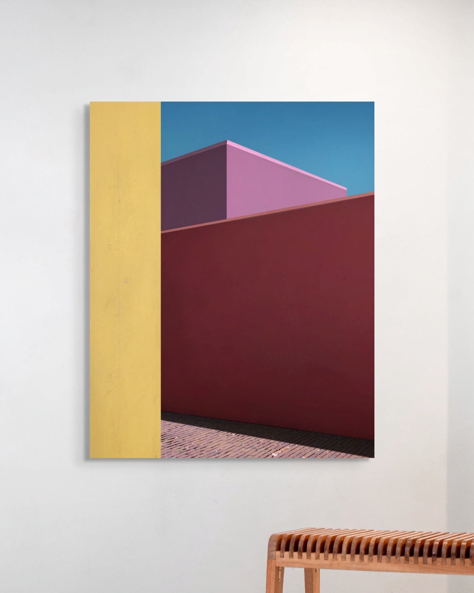 Abstract art piece with geometric shapes on a white wall above a wooden bench.