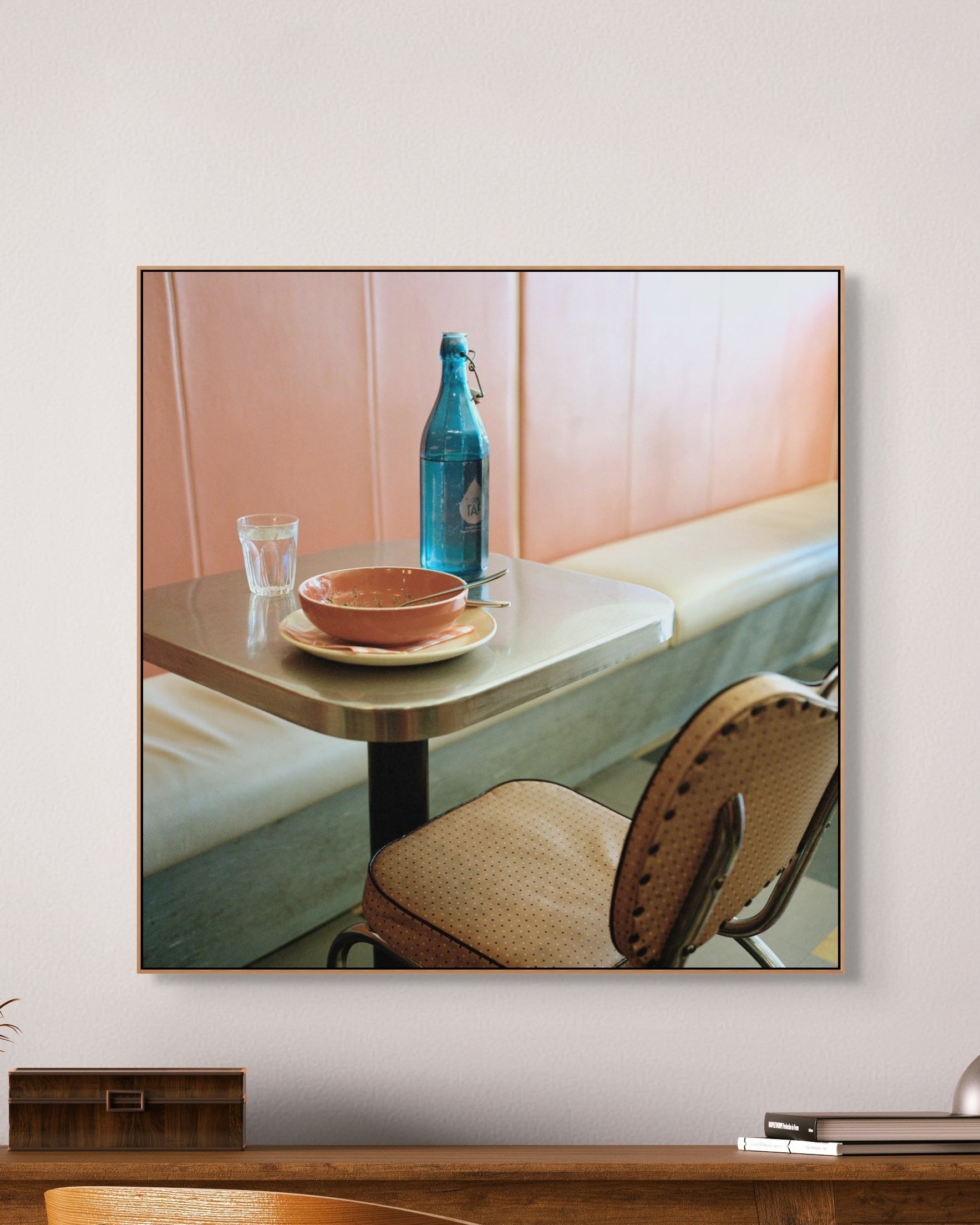 Framed artwork of a table setting with a bottle and bowl on a white wall.
