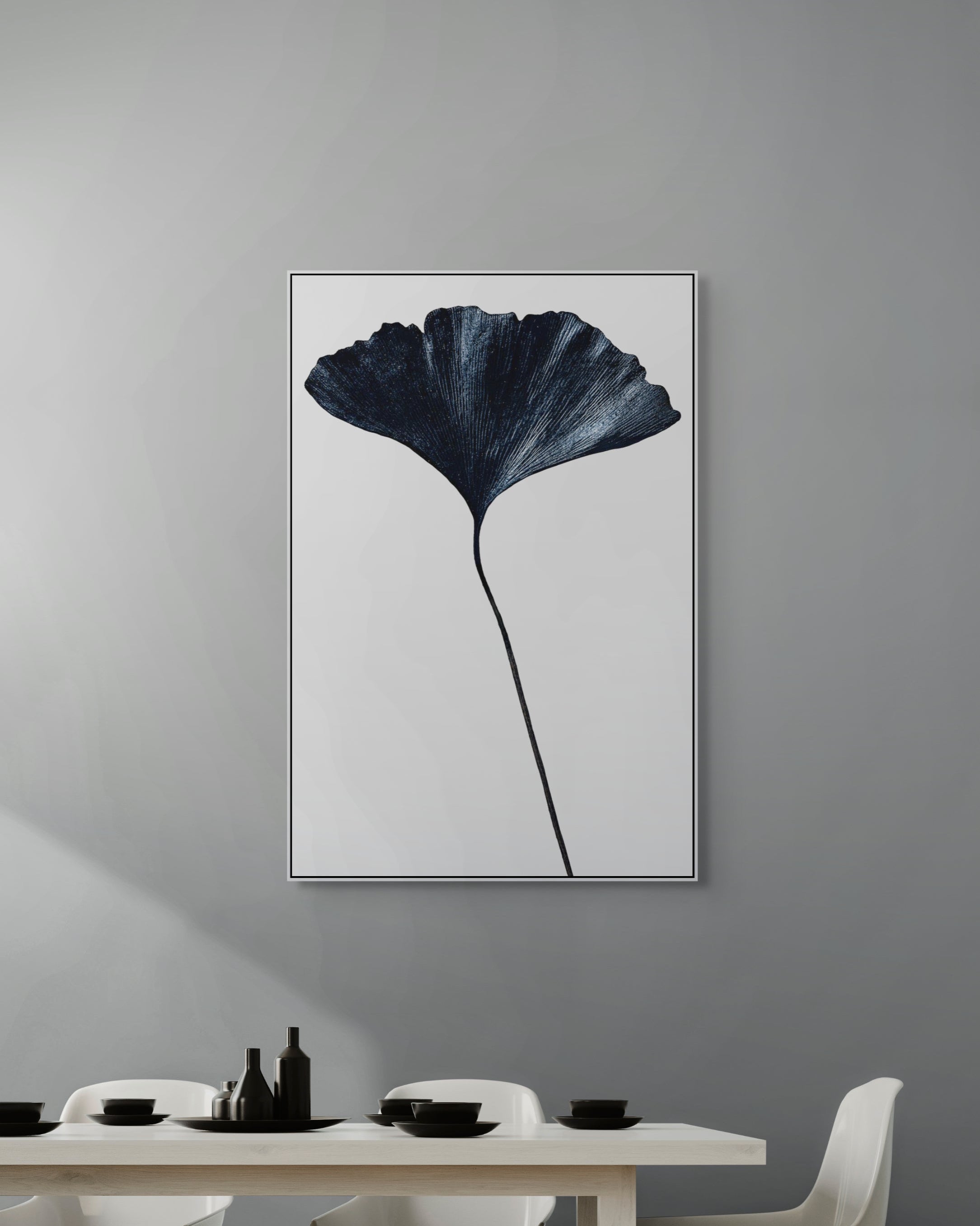 Framed artwork of a dark leaf on a gray wall above a dining table.