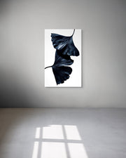 Framed artwork of black leaves on a white background hanging on a gray wall.