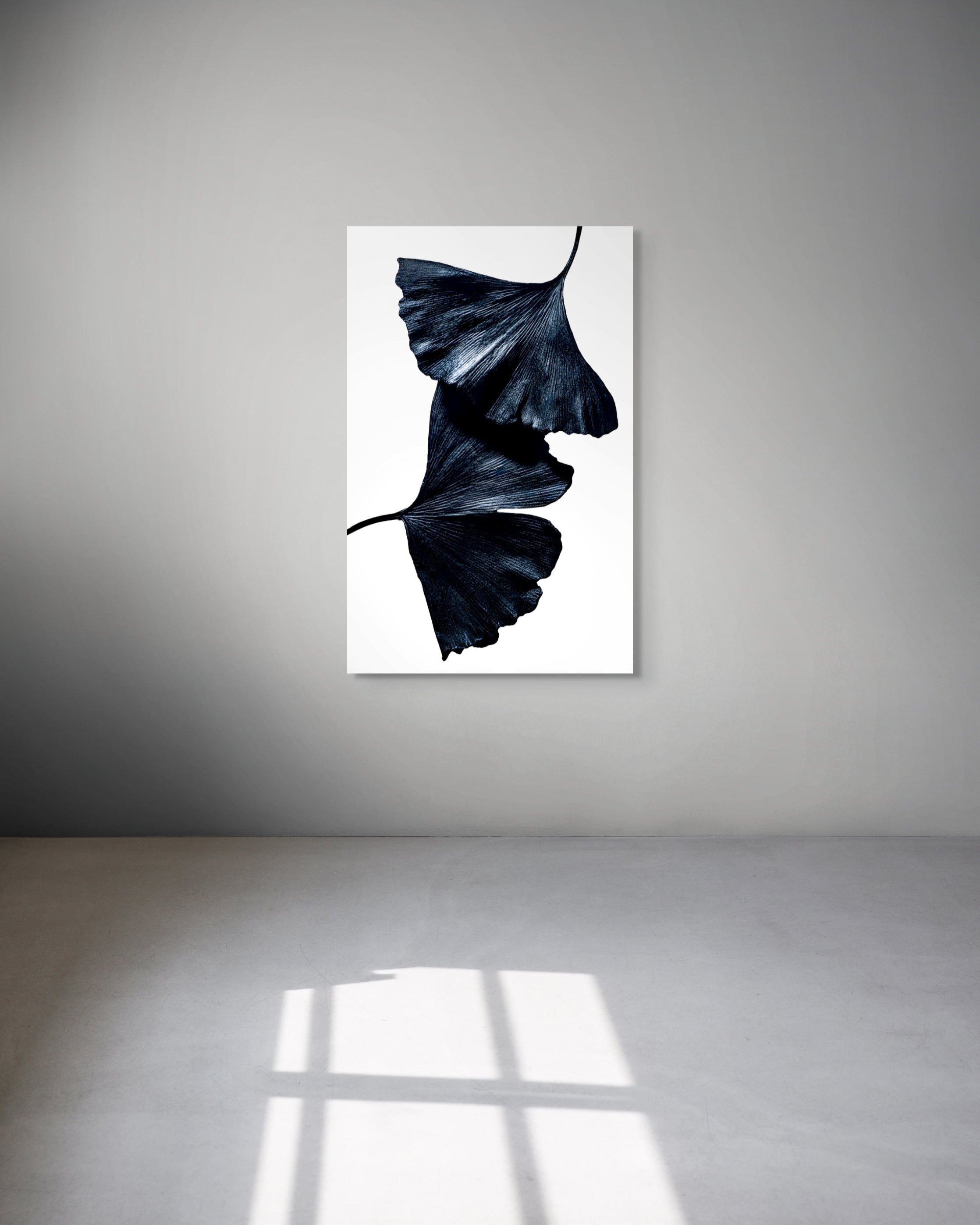 Framed artwork of black leaves on a white background hanging on a gray wall.