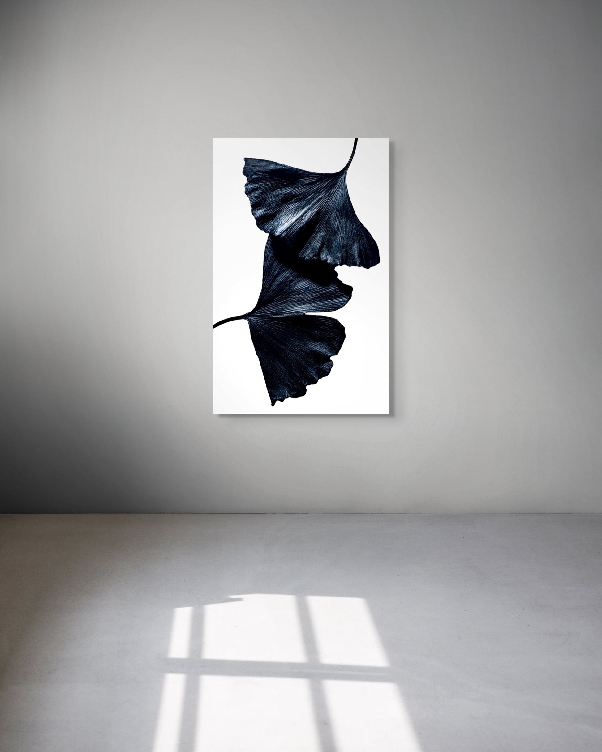 Metal print of black leaves on a white background hanging on a gray wall.