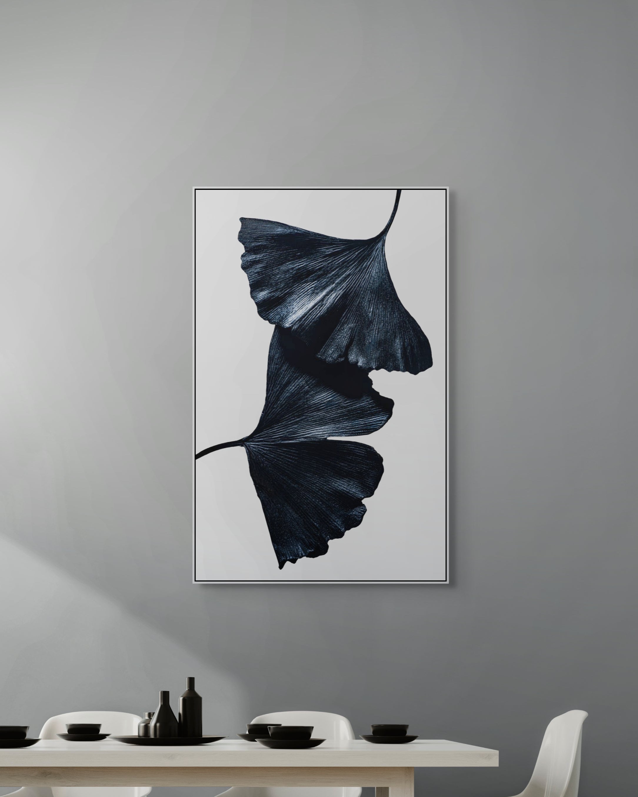 Framed artwork of a dark leaf on a gray wall above a dining table.