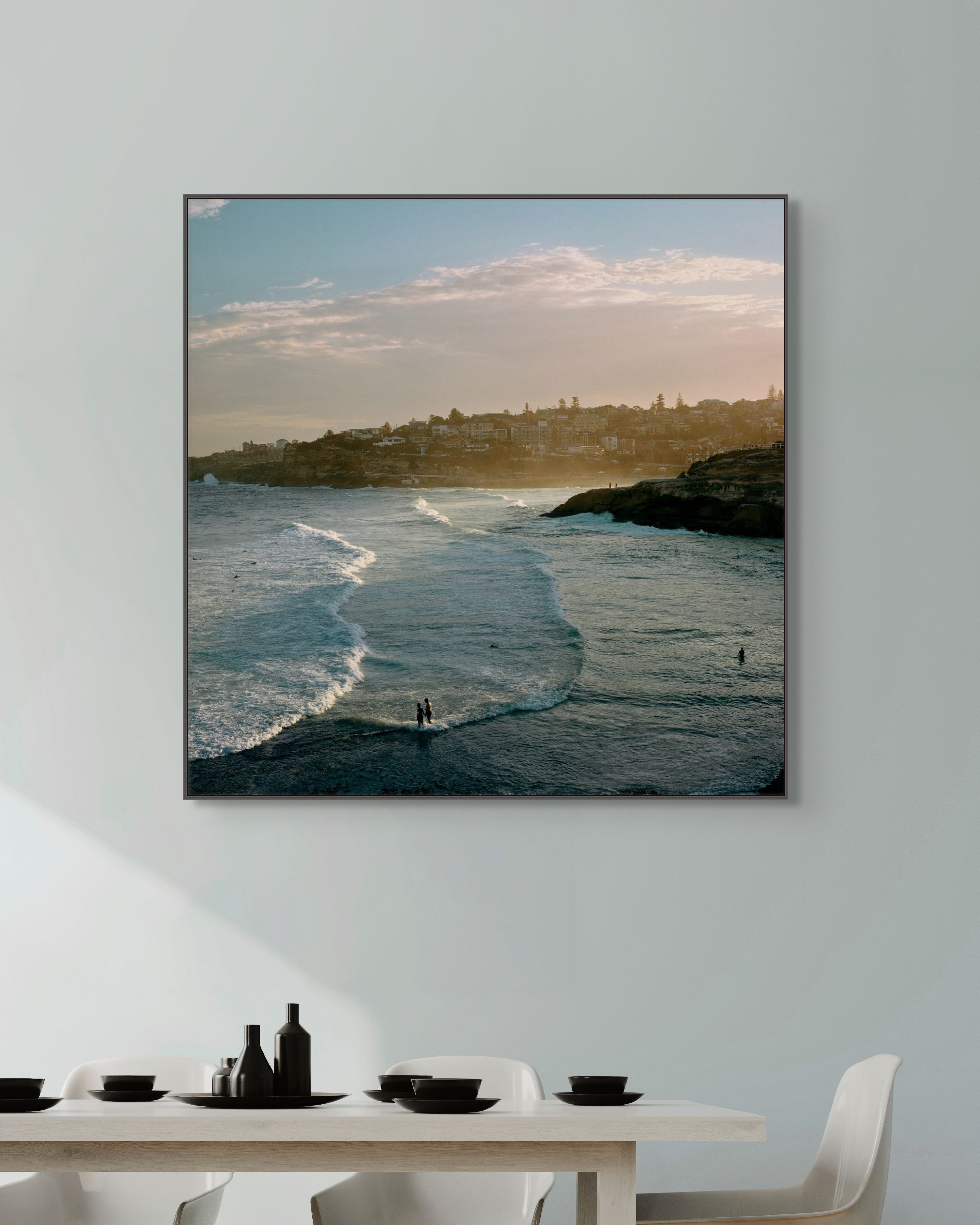 Framed artwork of a beach scene above a dining table with white chairs.