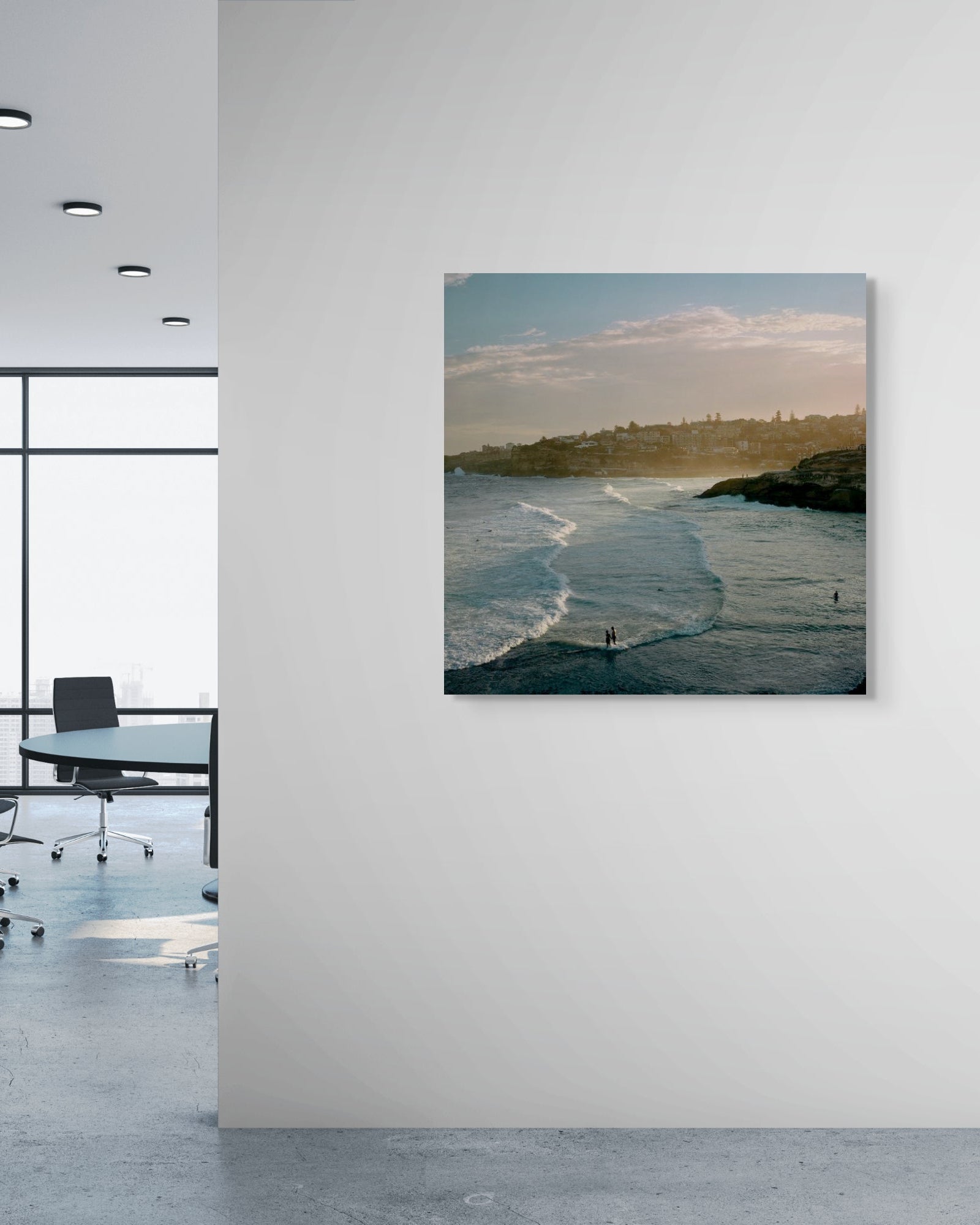 Metal print of a coastal landscape hanging on a light gray wall in a modern office with glass conference room.