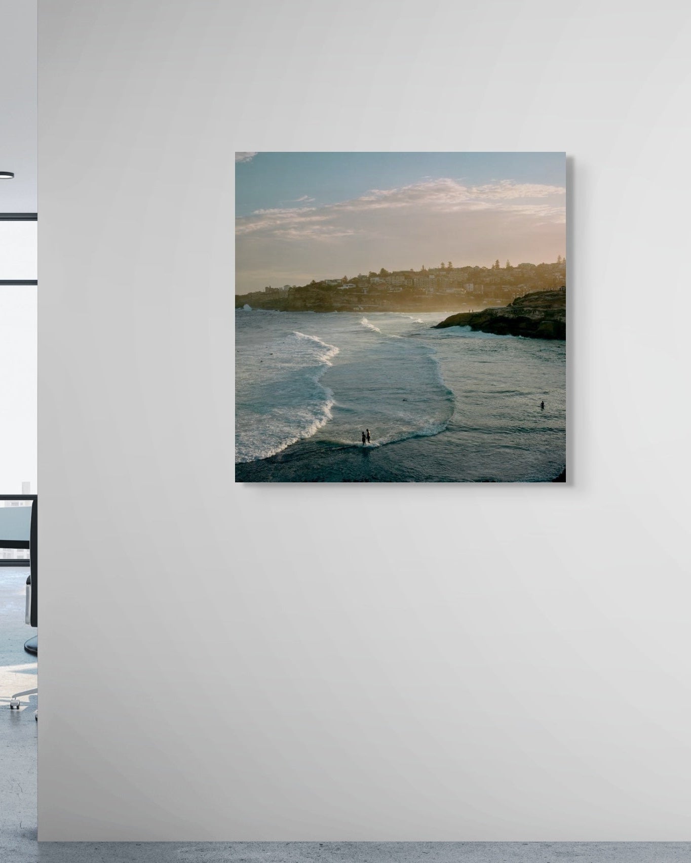 Metal print of a coastal scene with people in the water, hanging on a white wall in an office.