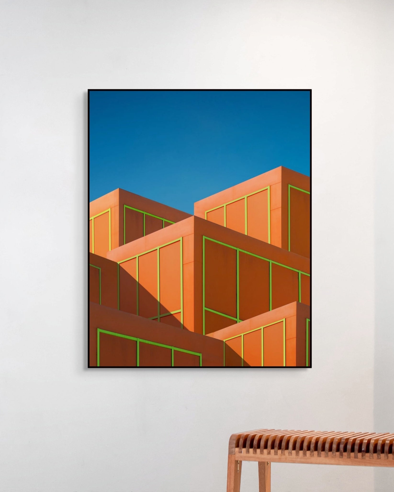 Framed abstract art of geometric shapes on a white wall with a wooden bench below.