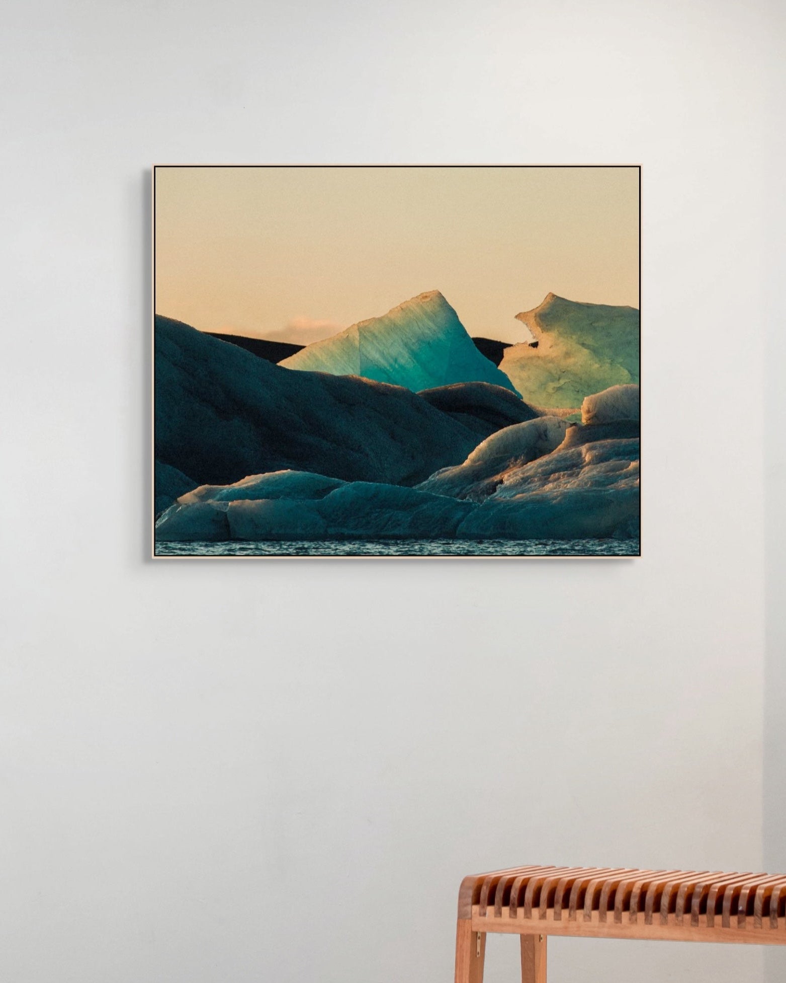 Framed artwork of icebergs on a white wall with a wooden bench below.