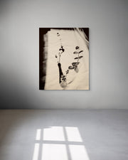 Framed artwork of a vase with leaves on a textured surface, displayed on a wall.