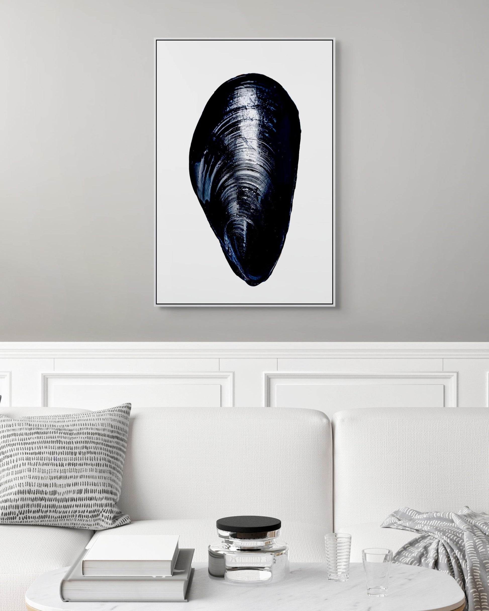 Framed artwork of a mussel shell on a gray wall above a white sofa.