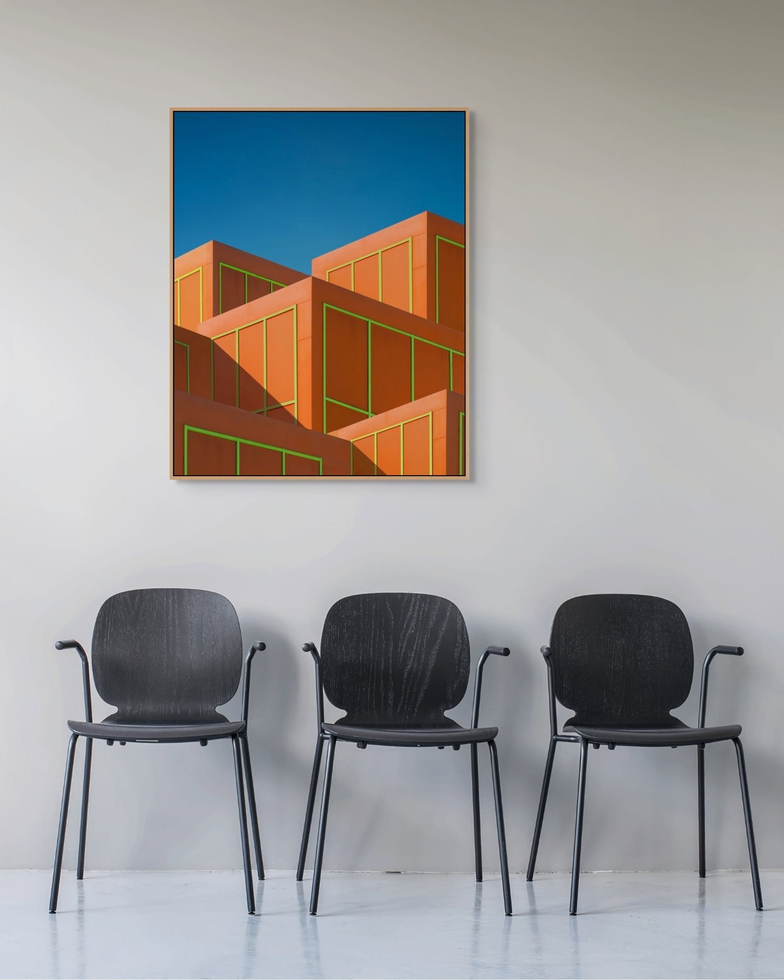 Framed Neon Boxes photograph by Marc Fischer above three black chairs in a minimalist interior.