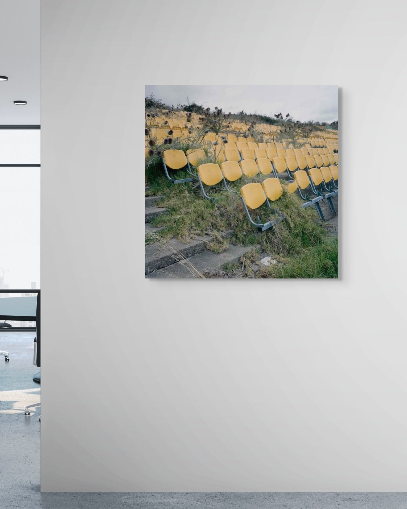 Art print of yellow chairs in a field on a white wall in an office.