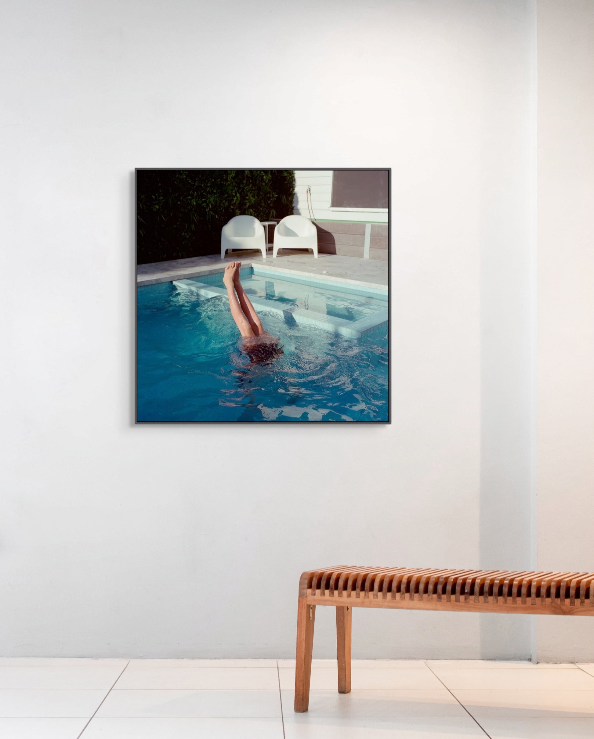 Framed artwork of a person swimming in a pool on a white wall above a wooden bench.
