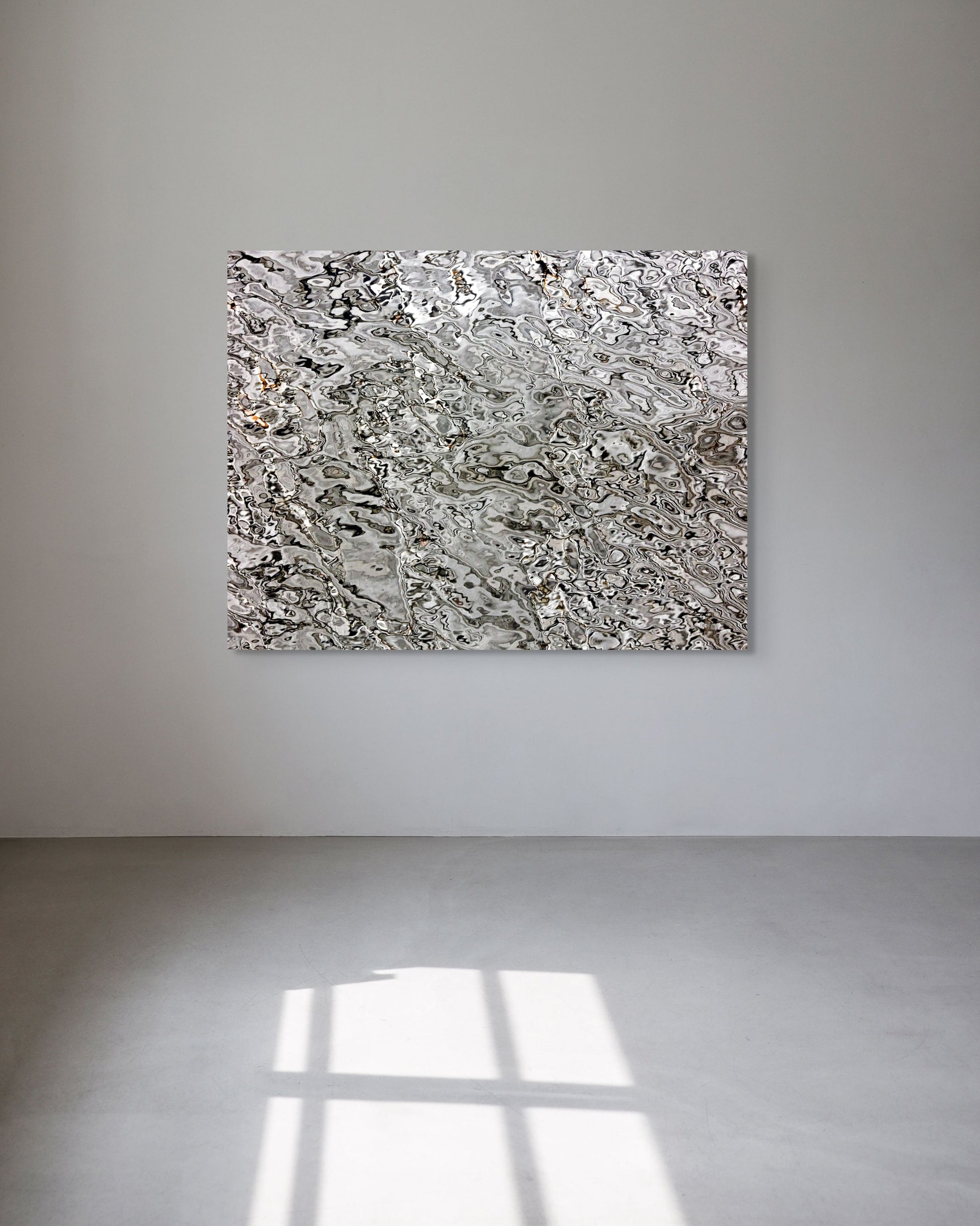 Abstract metal print on a white wall with sunlight casting shadows on the floor.