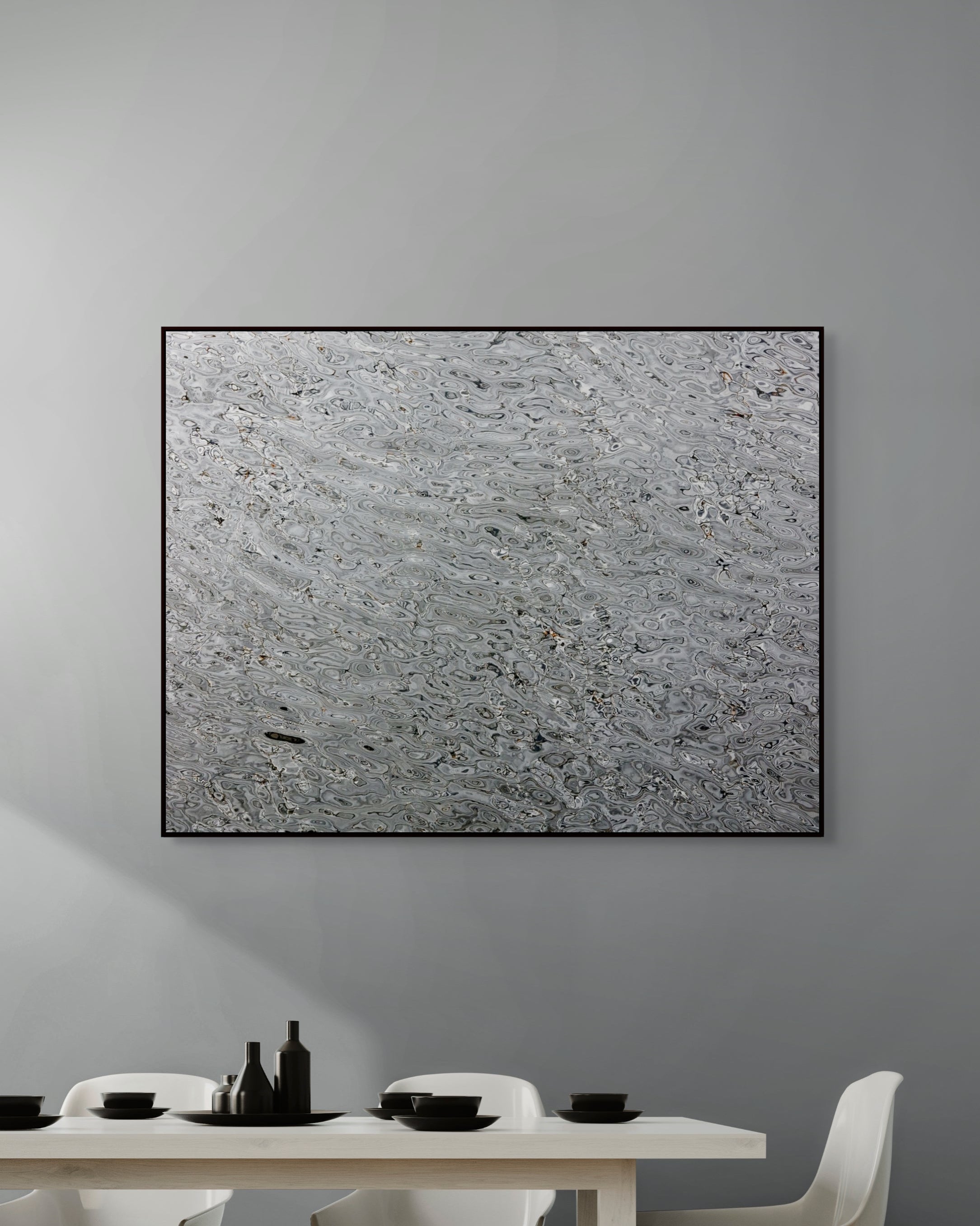 Abstract art piece on a gray wall above a dining table with white chairs.