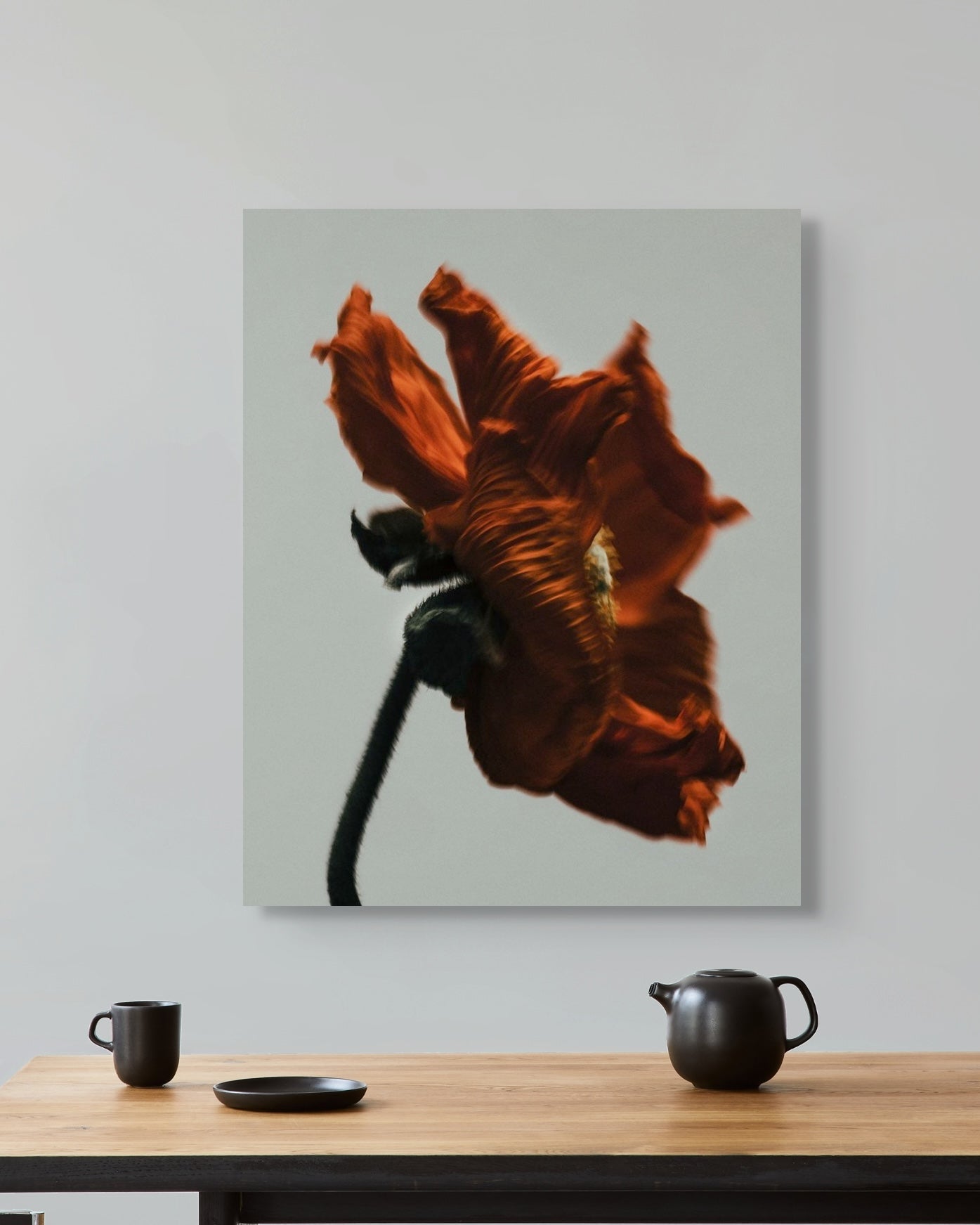 Metal print of a red flower on a wall above a wooden table with tea-making items.