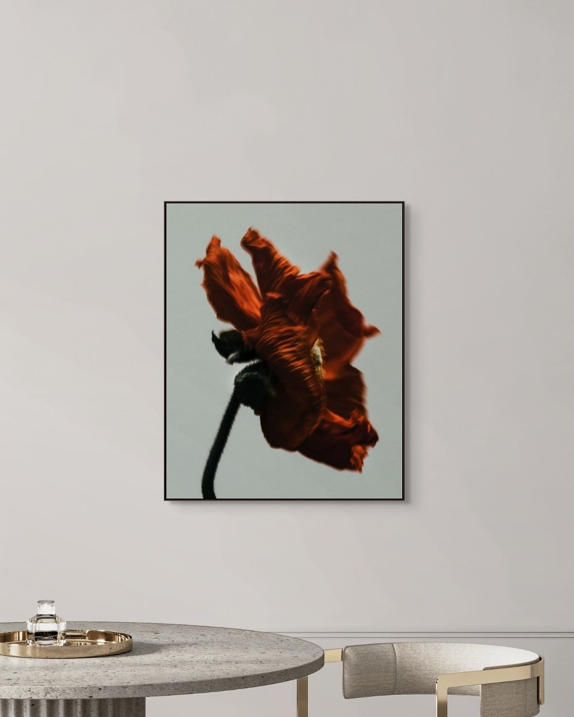 Framed artwork of a red flower on a gray wall above a round table.