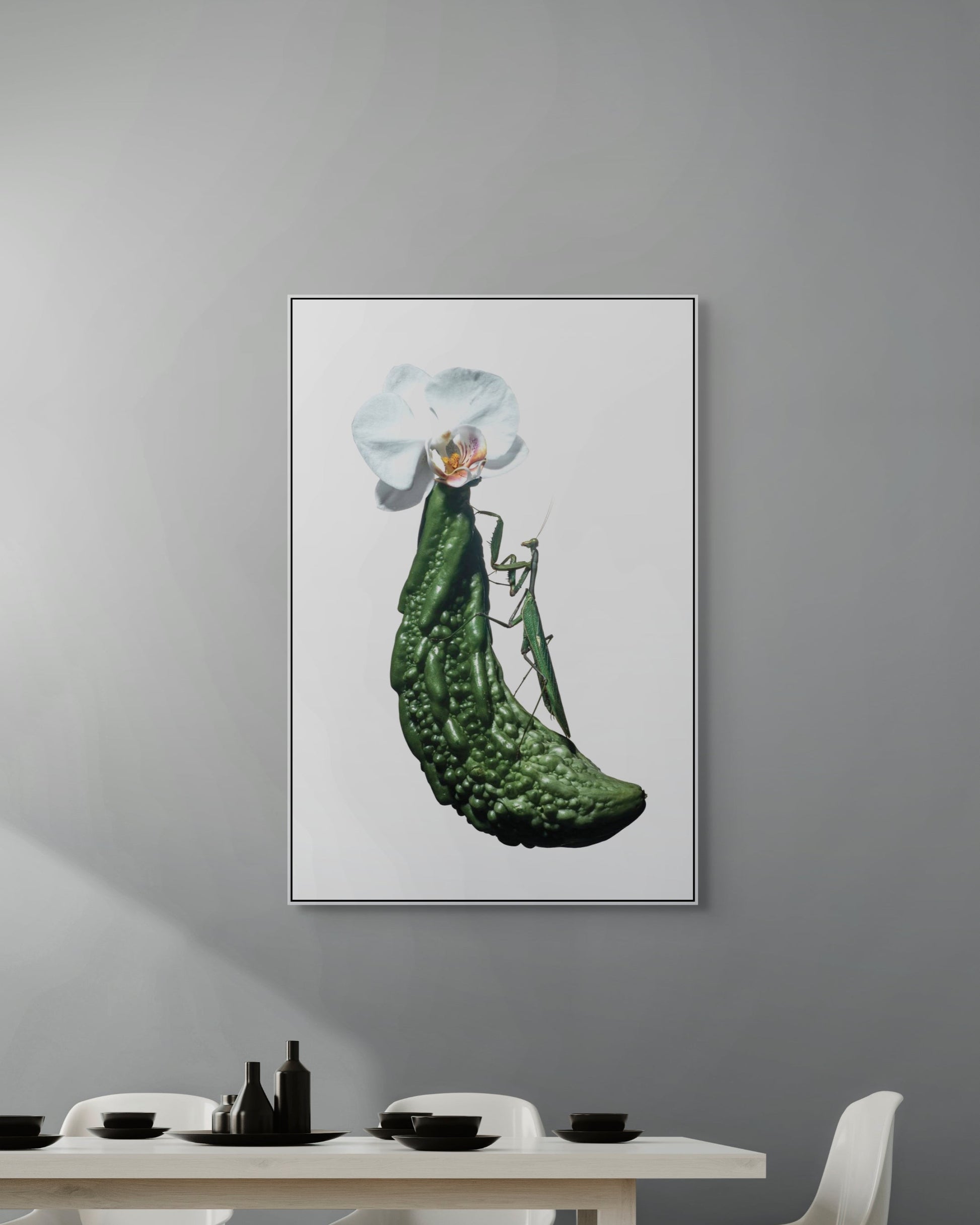 Framed artwork of a praying mantis with white flowers on a gray wall above a dining table.