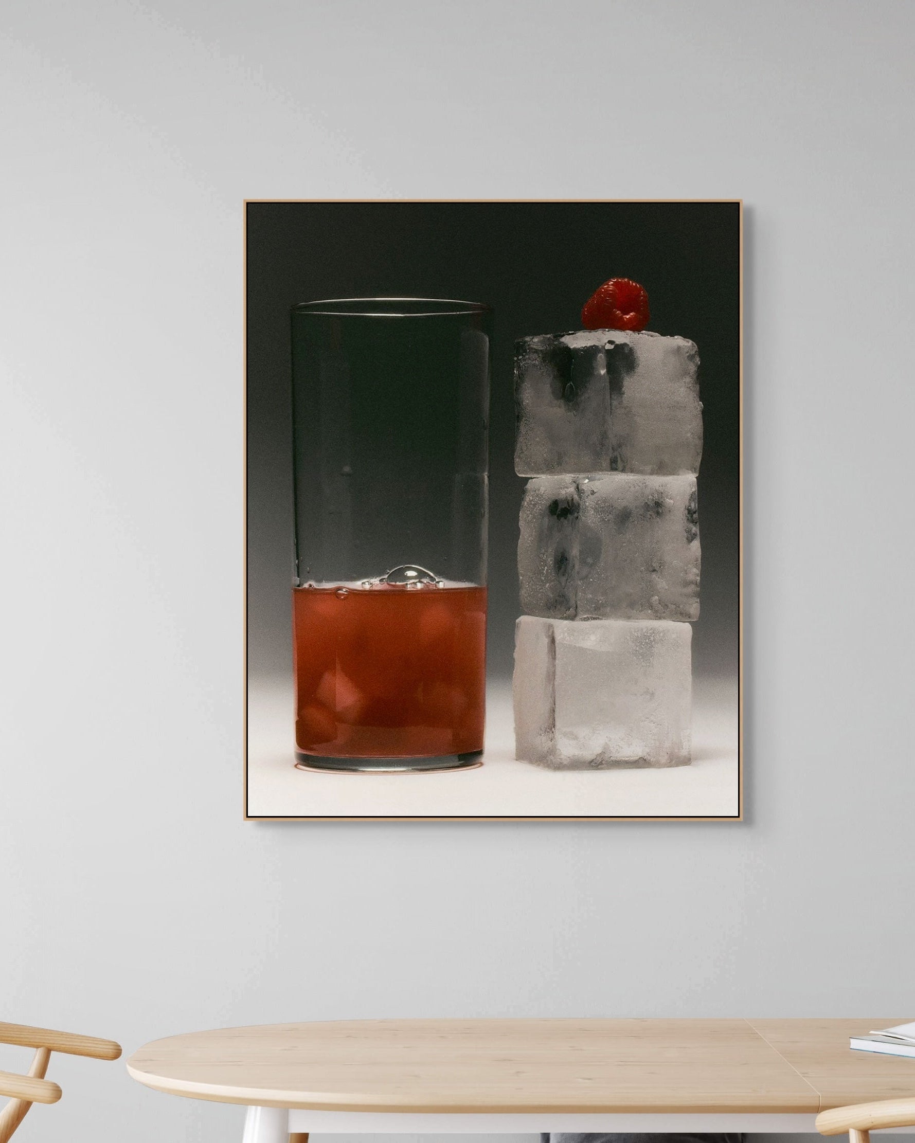 Framed artwork of a cocktail with ice and a cherry on a wall above a table.