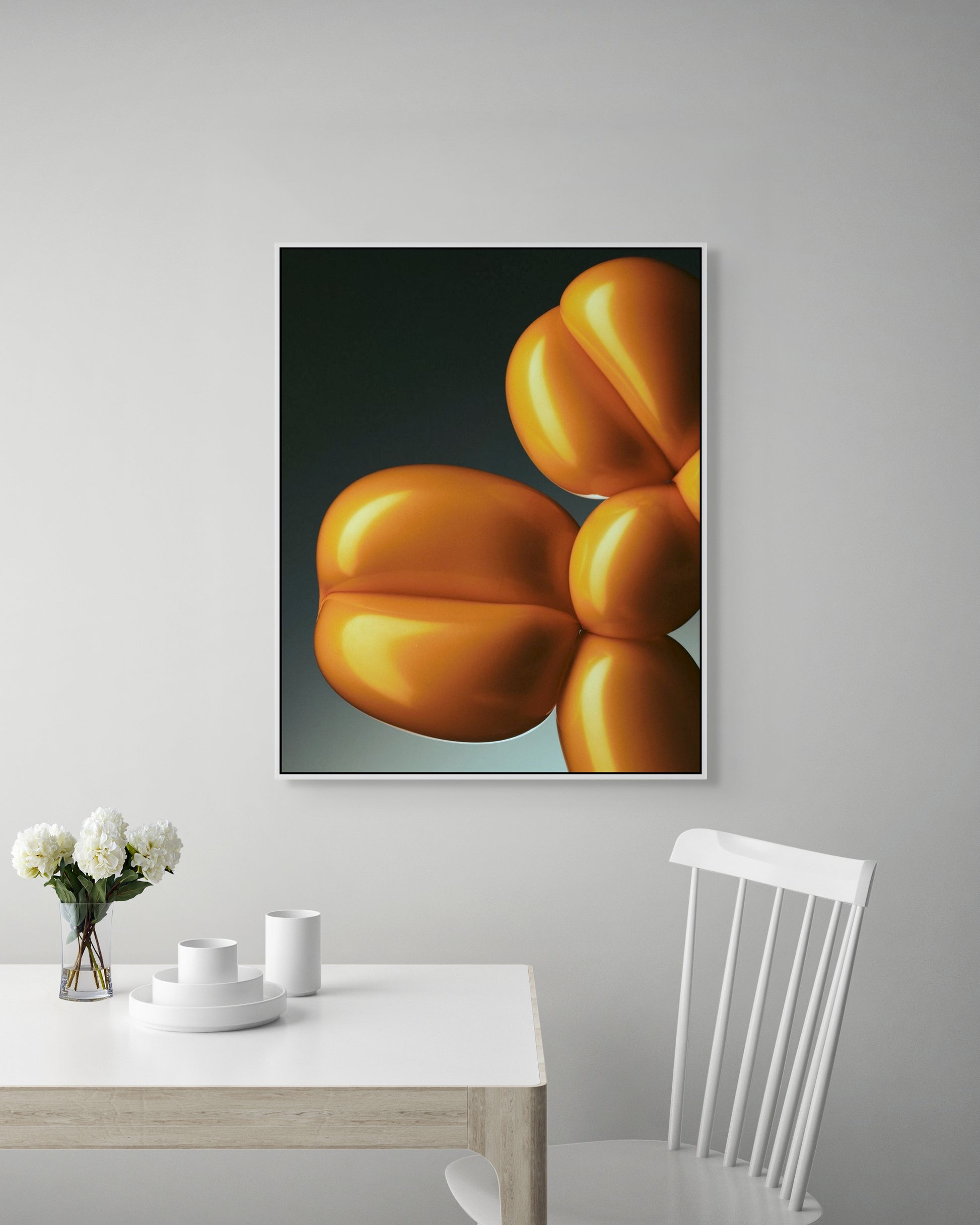 Framed artwork of a yellow still life on a gray wall above a white table with decor items.
