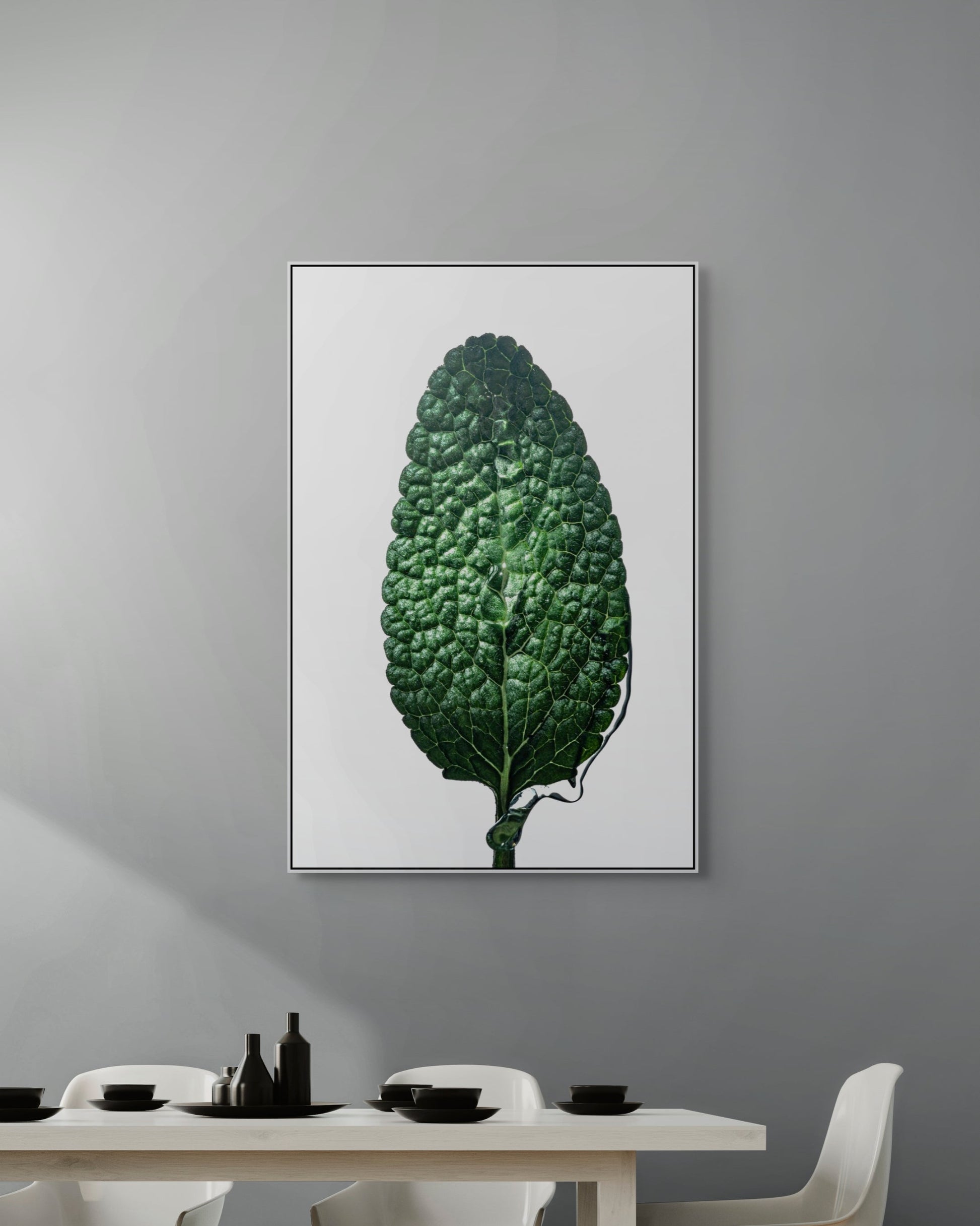 Framed artwork of a green leaf on a gray wall above a dining table.