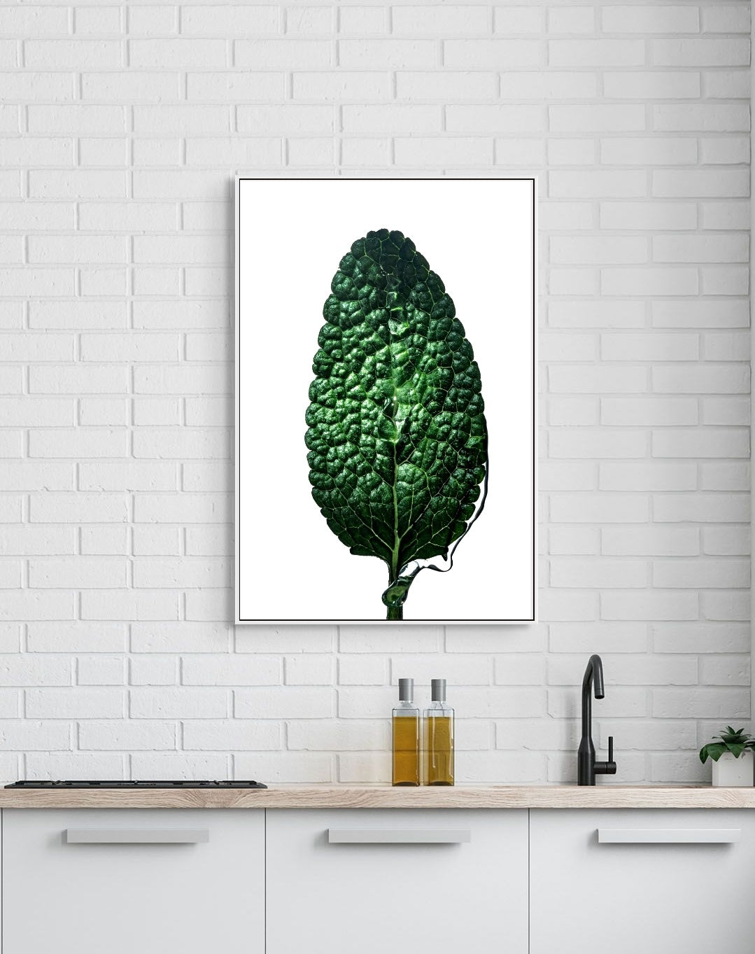Framed artwork of a green leaf on a kitchen wall with white tiled backsplash.