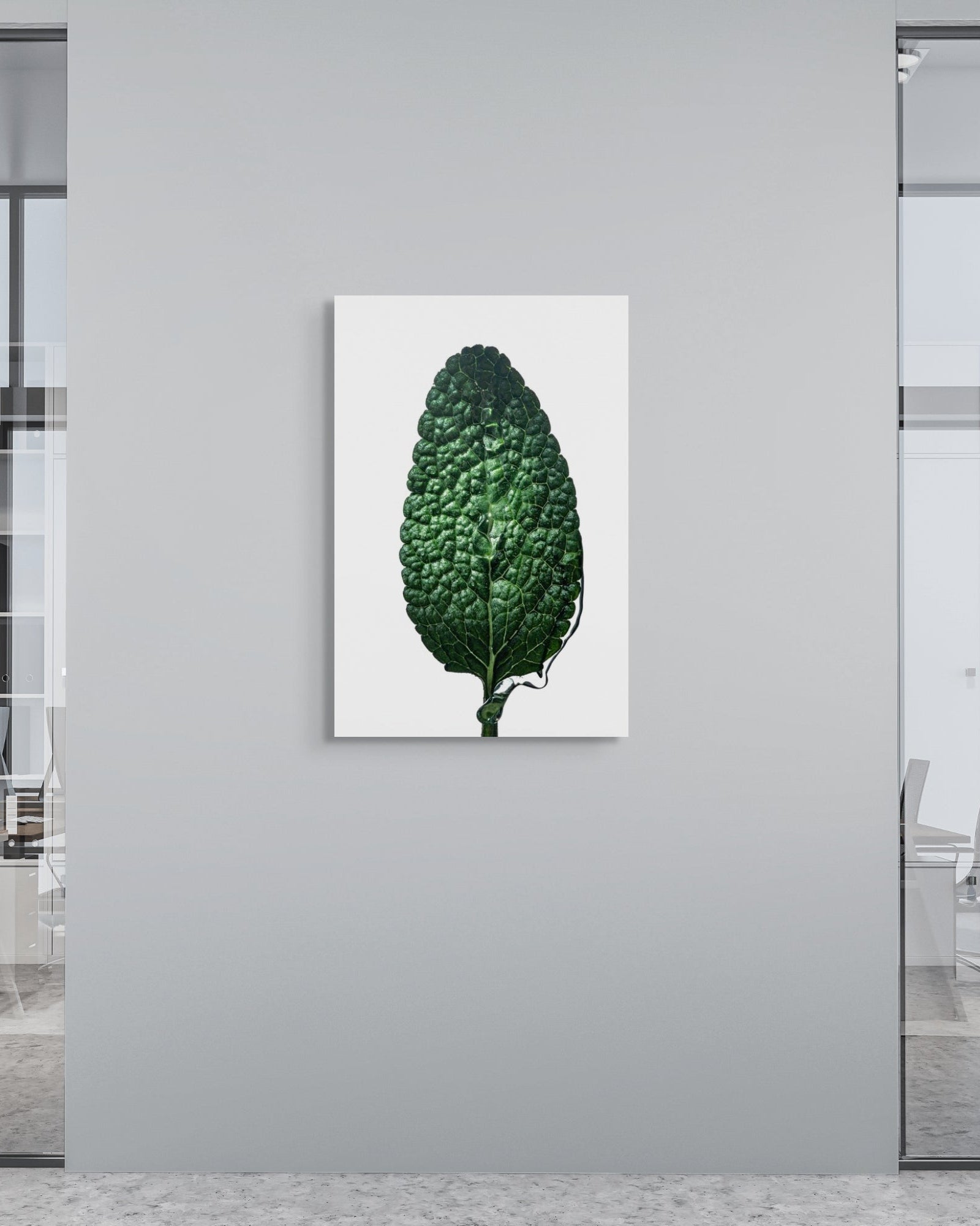 Sage leaf metal print on a gray wall in an office setting with glass walls and chairs.
