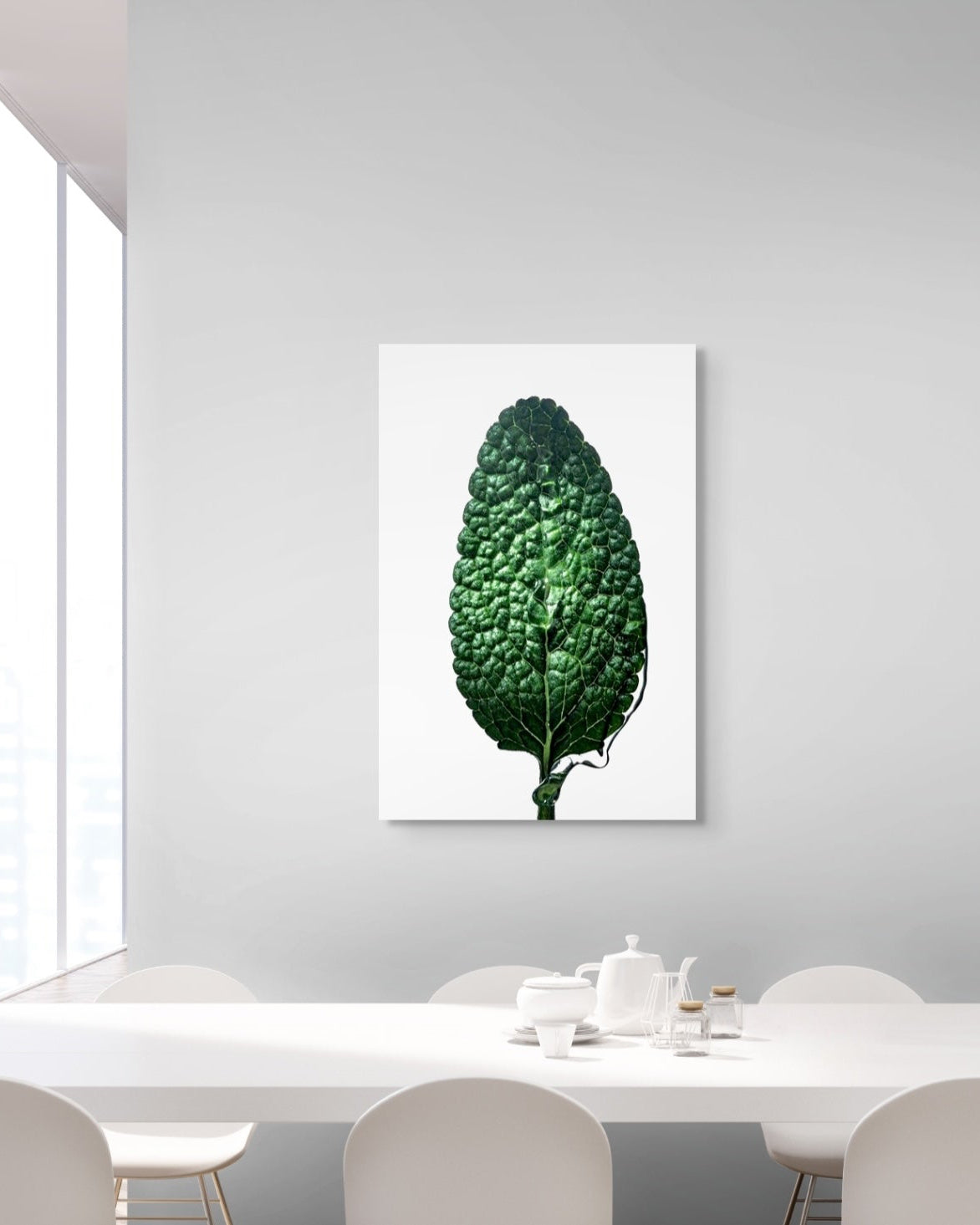 Framed artwork of a green leaf on a white wall above a dining table.