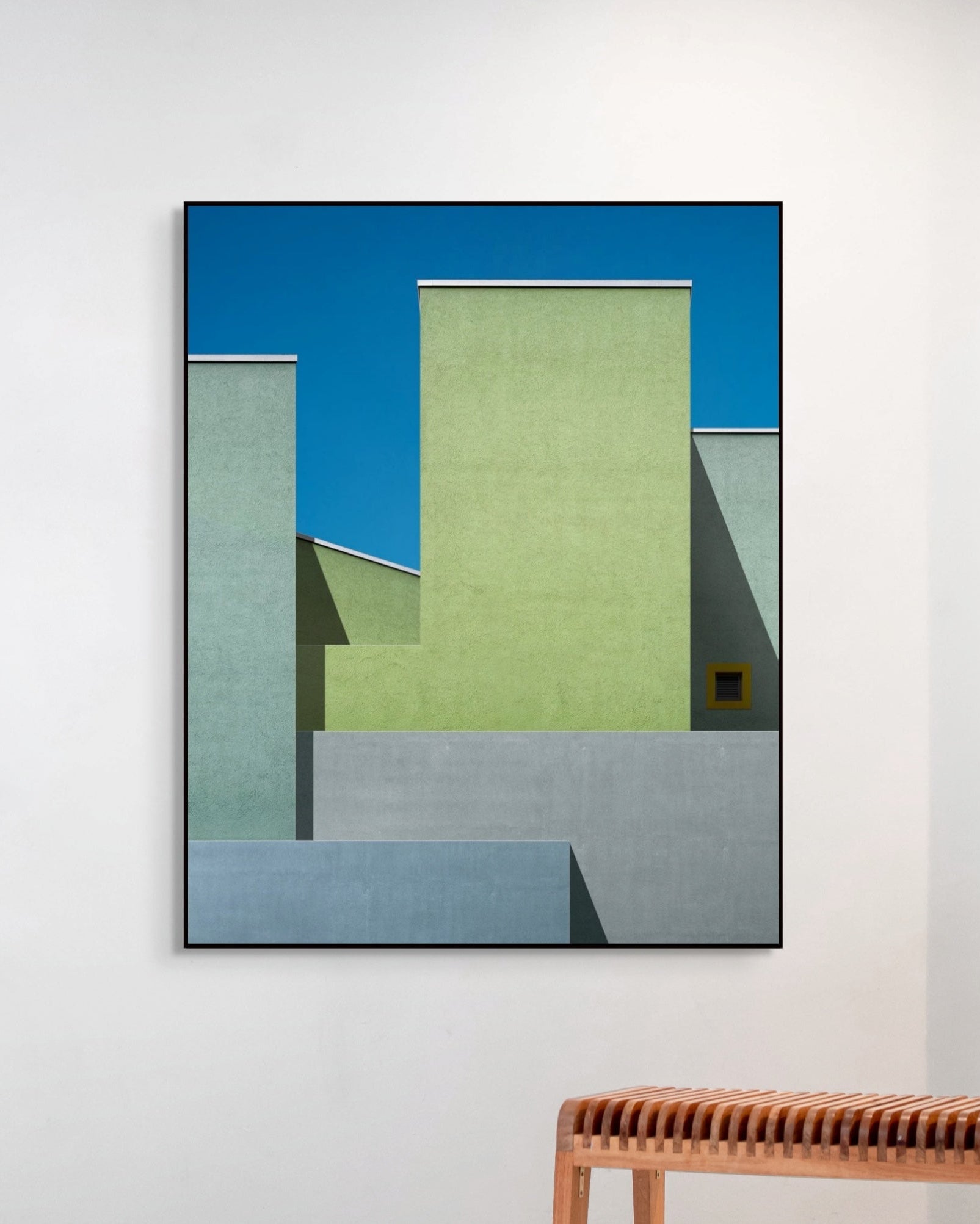 Abstract geometric art piece on a white wall with a wooden bench below.