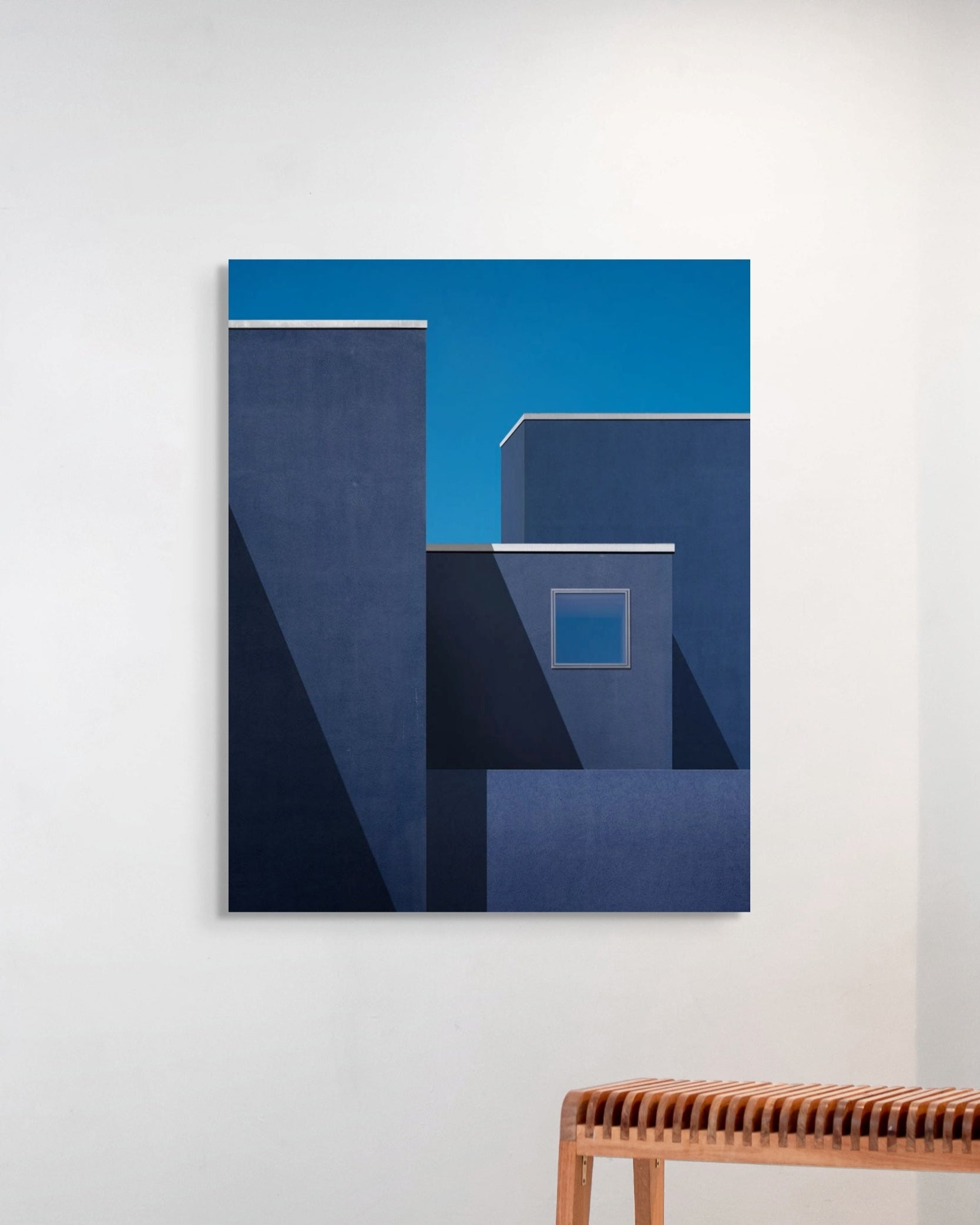 Abstract blue artwork on a white wall with a wooden bench below